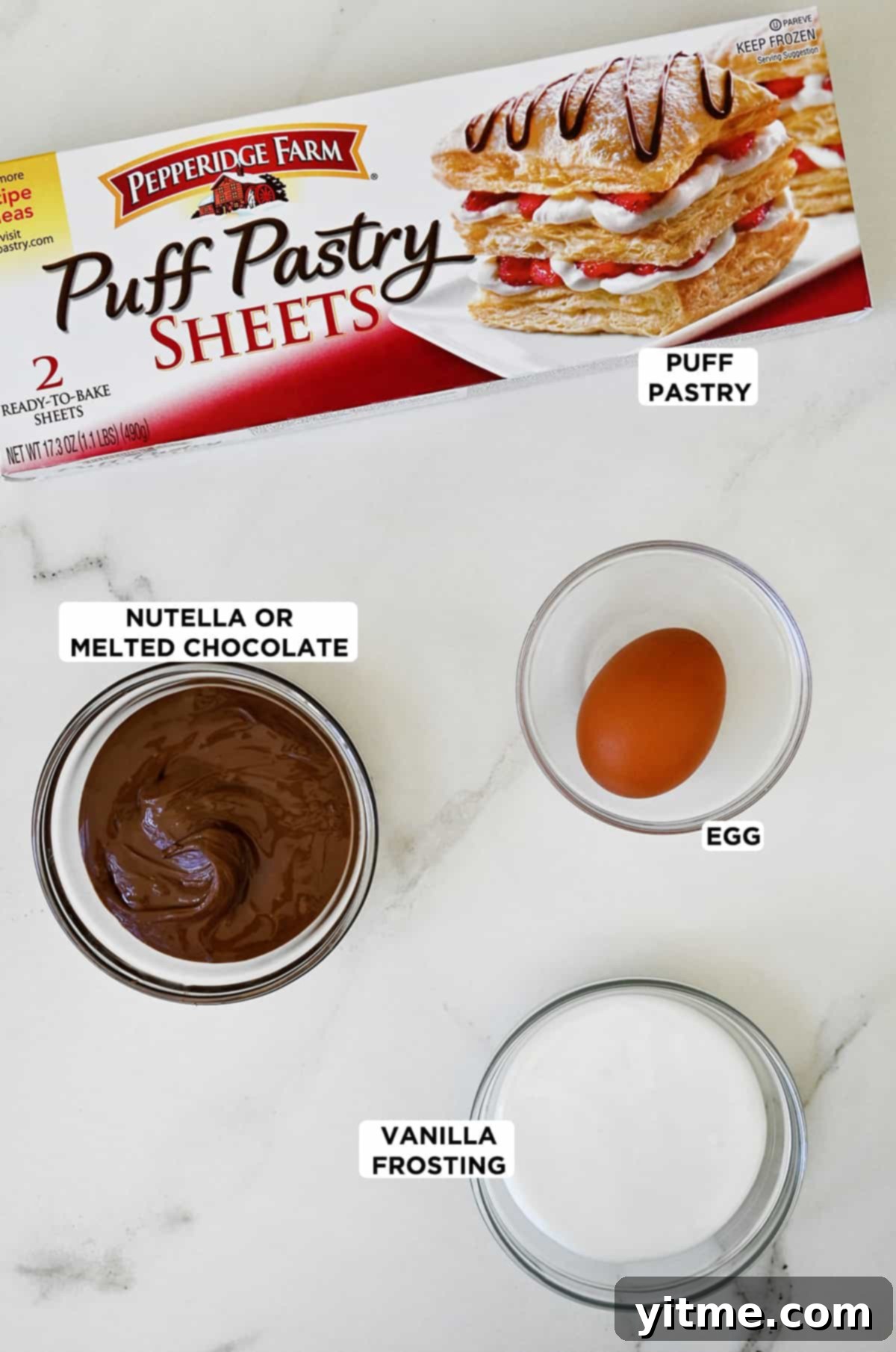 A box of puff pastry sheets next to three glass bowls containing Nutella, an egg and vanilla frosting, ready for baking.