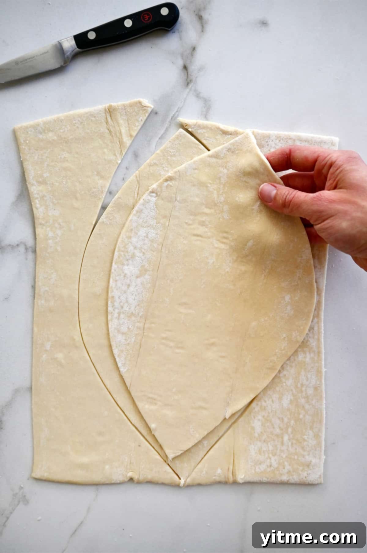 A hand holds a football-shaped piece of puff pastry over a rectangular puff pastry piece to trace.