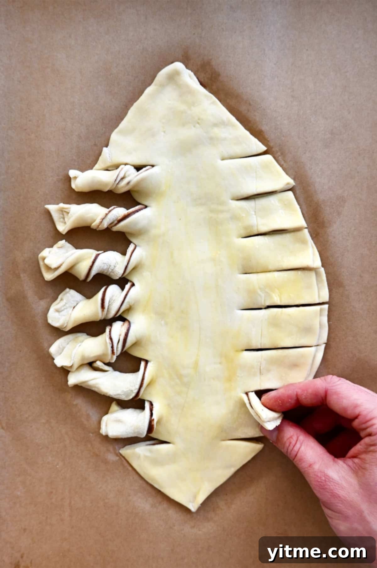 Puff pastry in the shape of a football with twisted edges on a parchment paper-lined baking sheet.