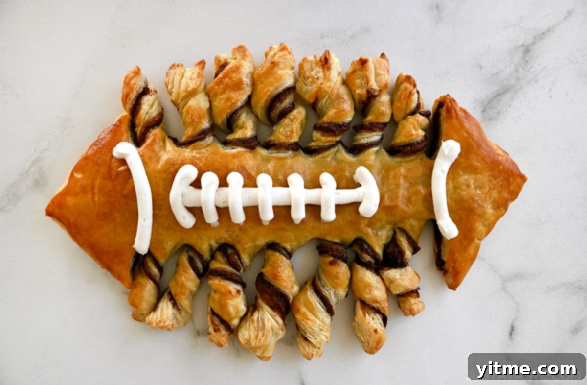 A puff pastry football with vanilla frosting laces on a marble countertop, ready to be enjoyed.