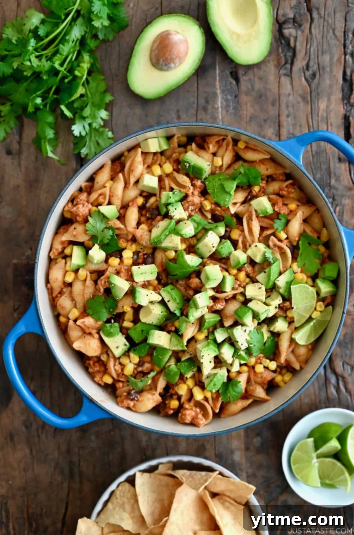 Cheesy Turkey Taco Pasta topped with avocado and chopped fresh cilantro next to a small plate with slices of limes.