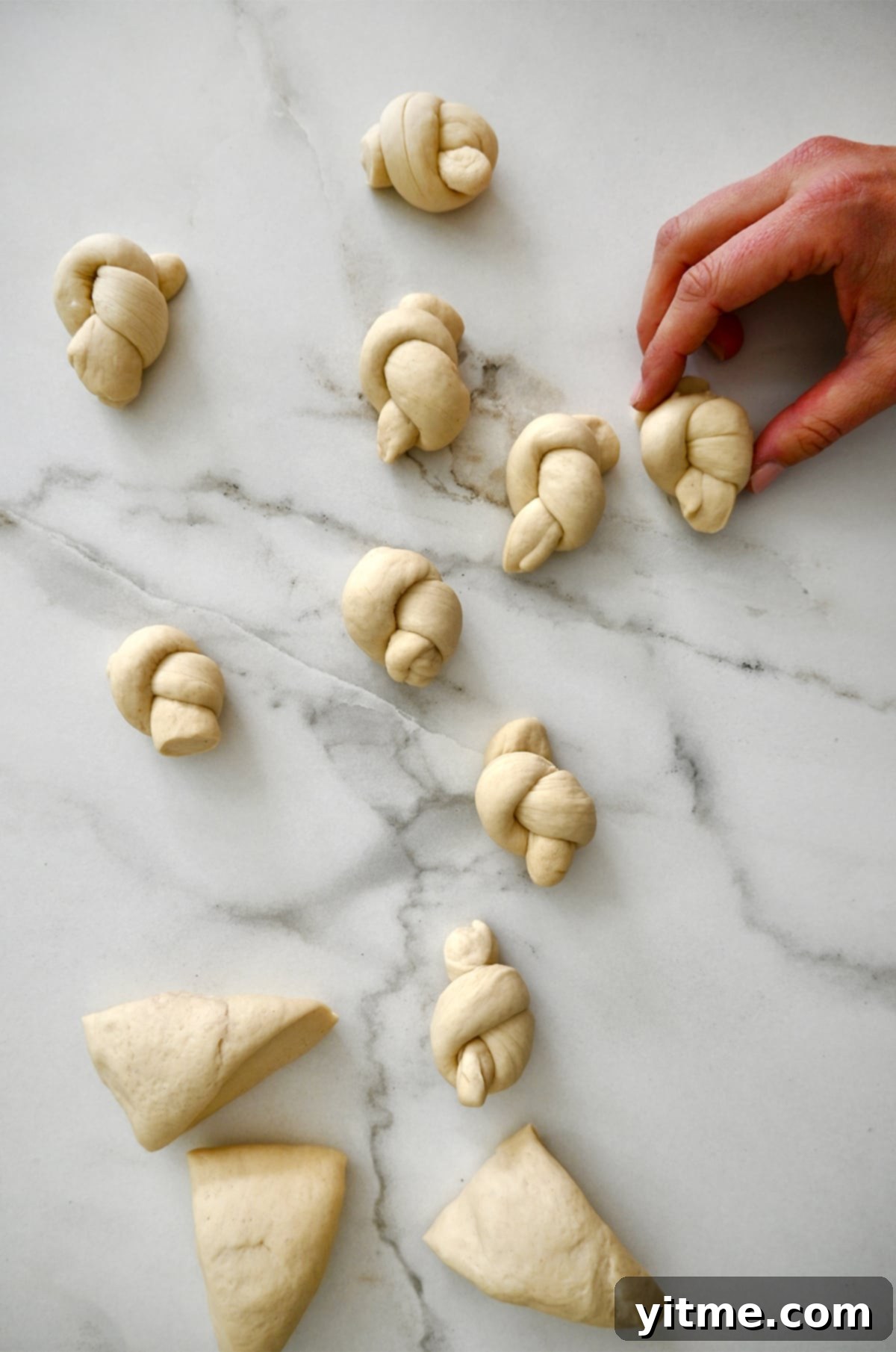 Several portions of pizza dough expertly shaped into classic pretzel knots, ready for the next step, displayed on a smooth marble surface.