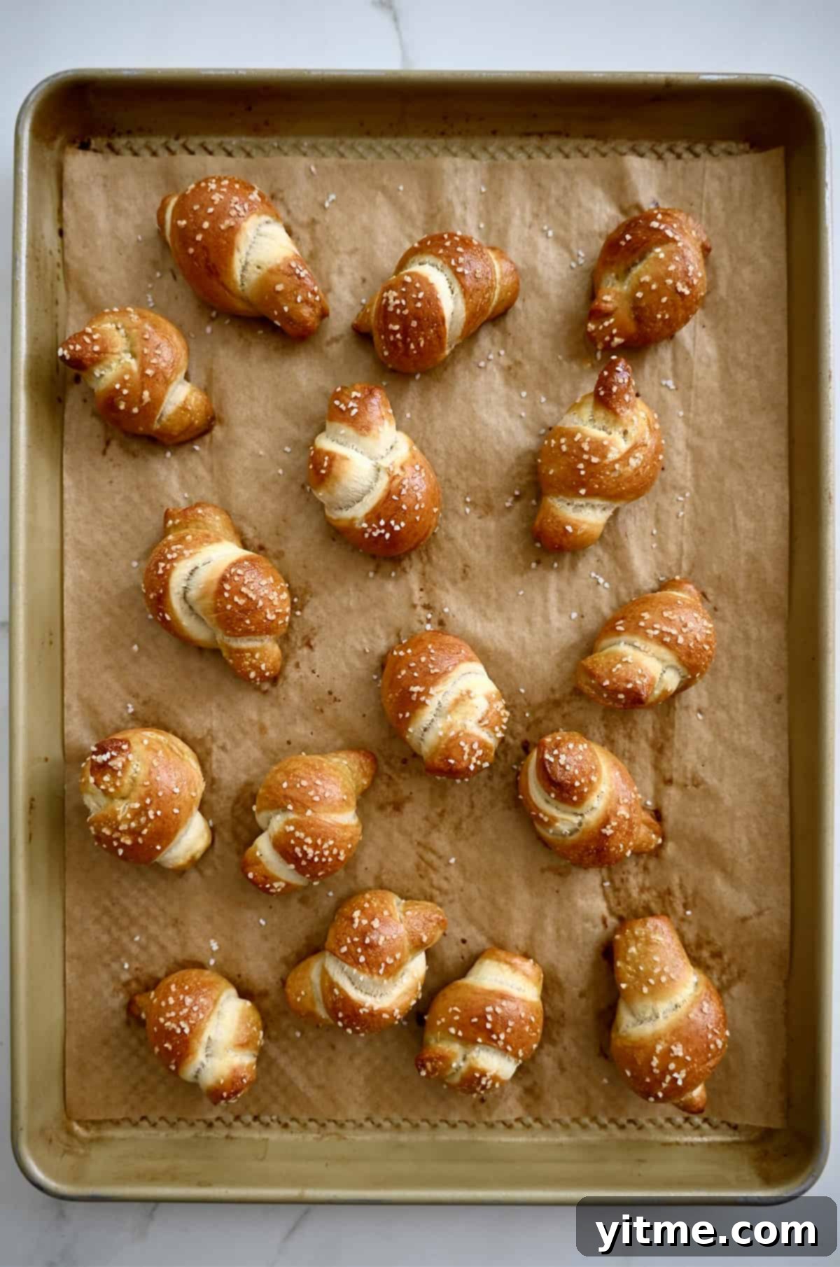 A close-up view of perfectly golden brown soft pretzel knots cooling on a parchment paper-lined baking sheet, showcasing their appealing texture.