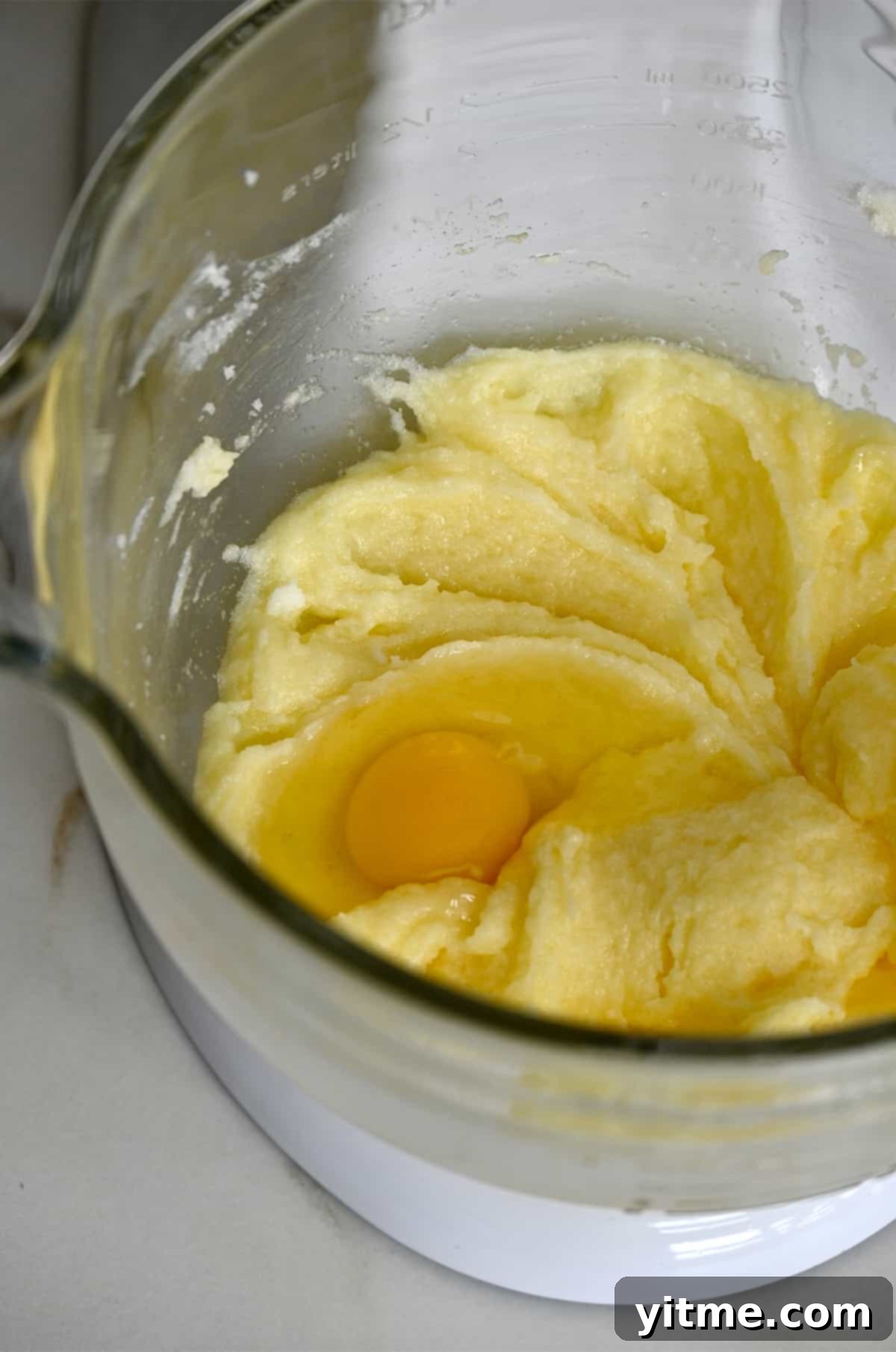 A raw egg atop cake batter in a bowl of a stand mixer.