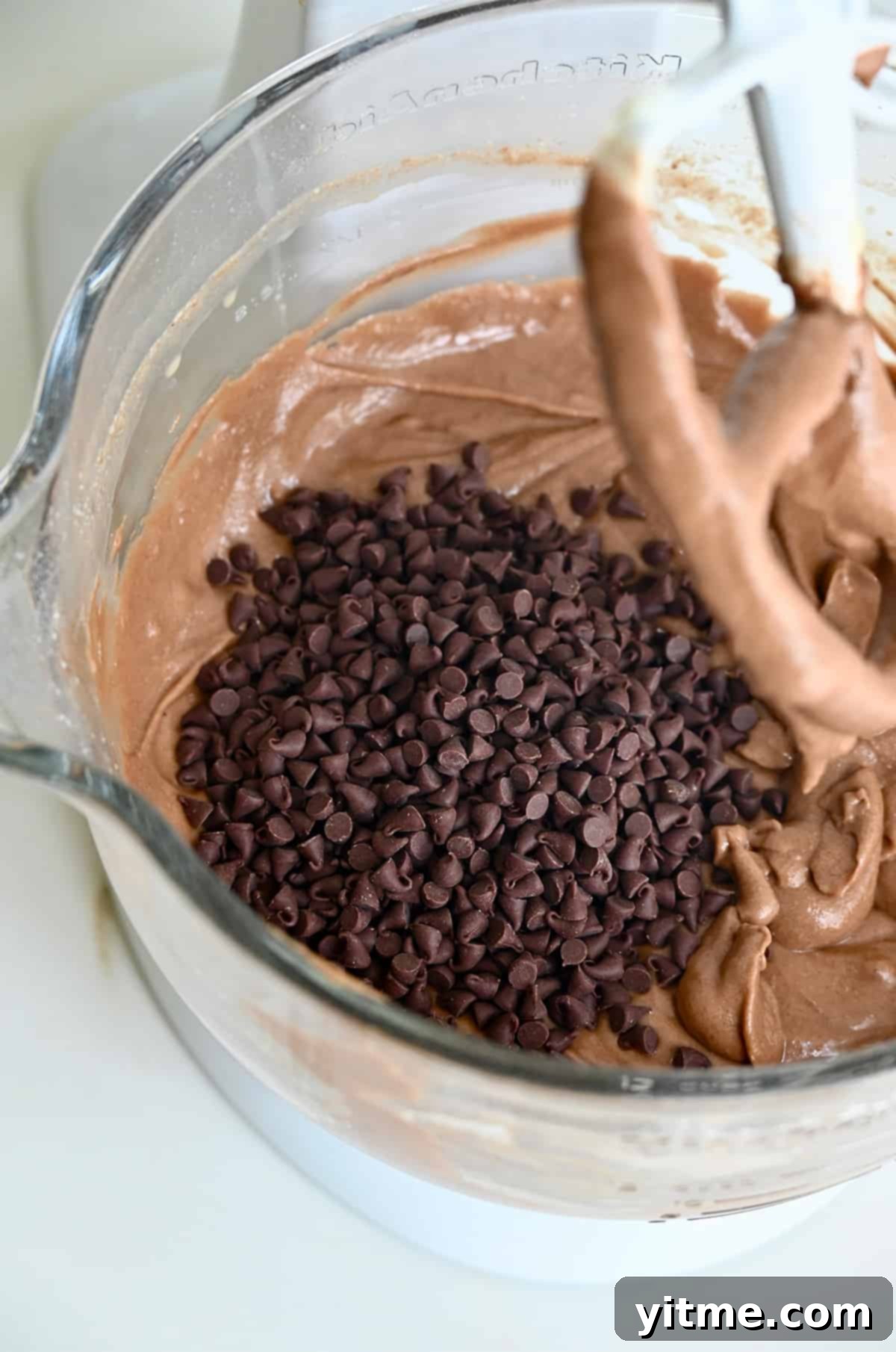 Mini chocolate chips in chocolate cake batter in a bowl of a stand mixer.