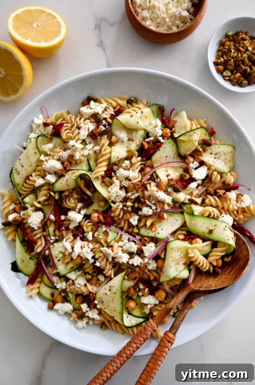 A top-down view of Zucchini Pasta Salad with feta cheese, chickpeas, sun-dried tomatoes and pistachios in a large serving bowl with wooden spoons