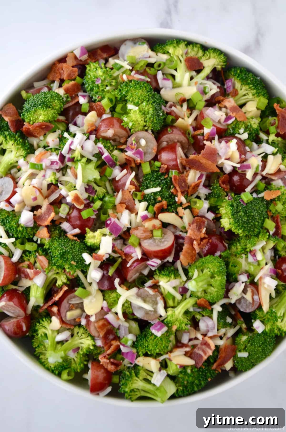 A top-down view of a large bowl containing broccoli grape salad with shredded mozzarella cheese and bacon crumbles.