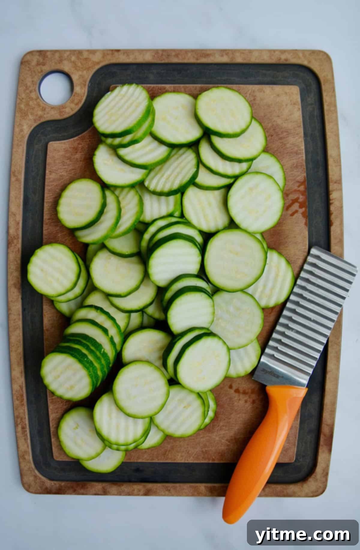 Crinkle cut zucchini slices on a cutting board next to a sharp crinkle cut knife.