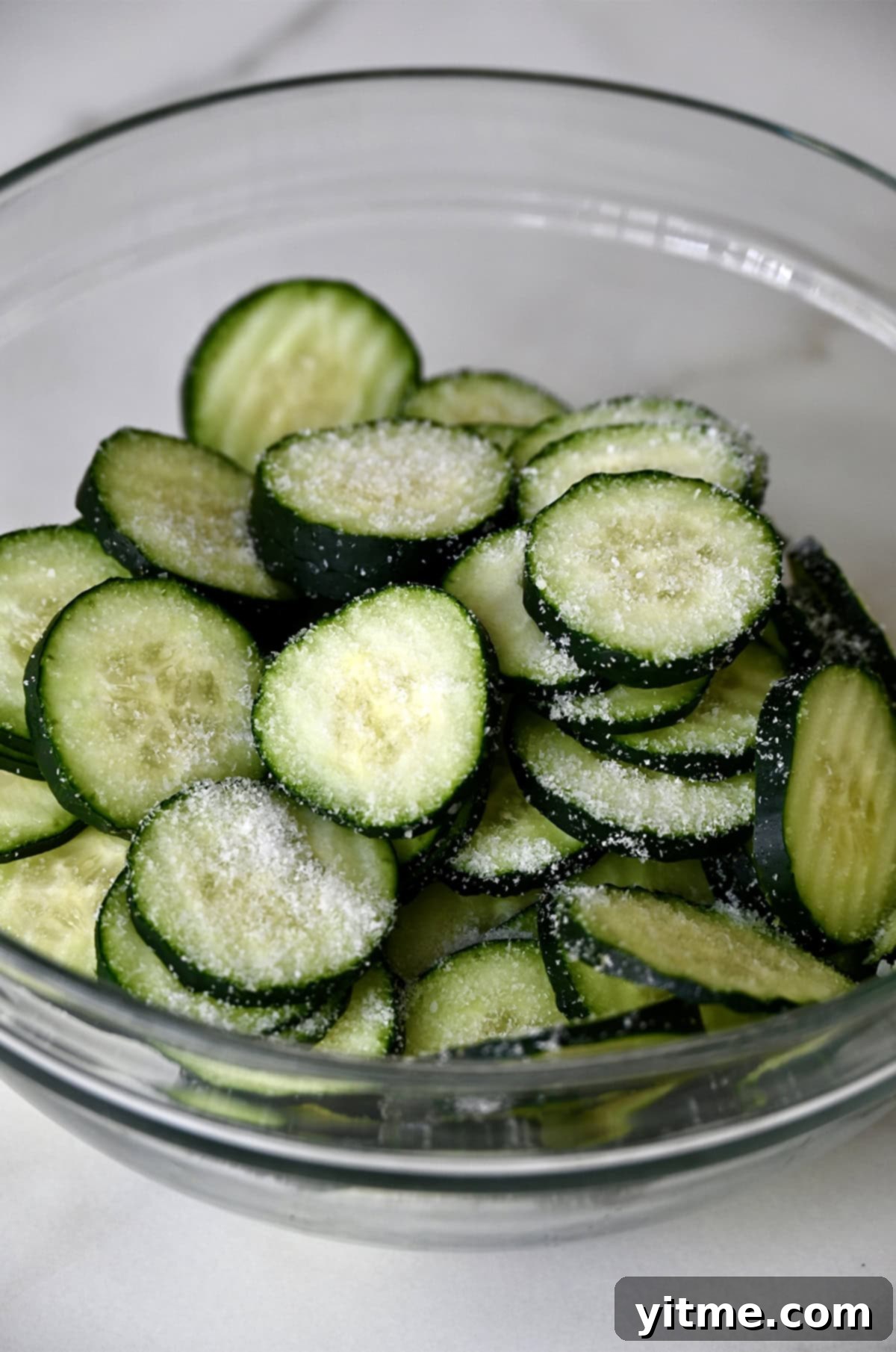 Zucchini slices with salt in a glass bowl. Drawing out moisture for crisp pickles.