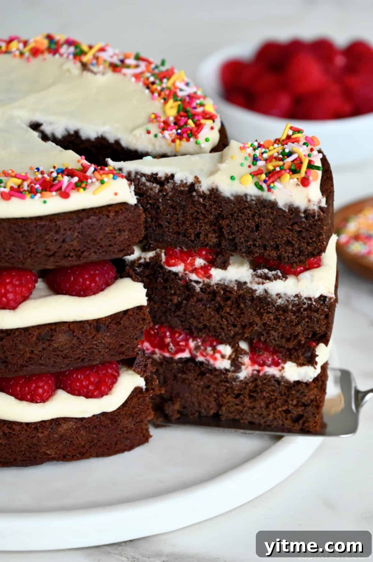 A three-tiered chocolate cake with cream cheese frosting and fresh raspberries.