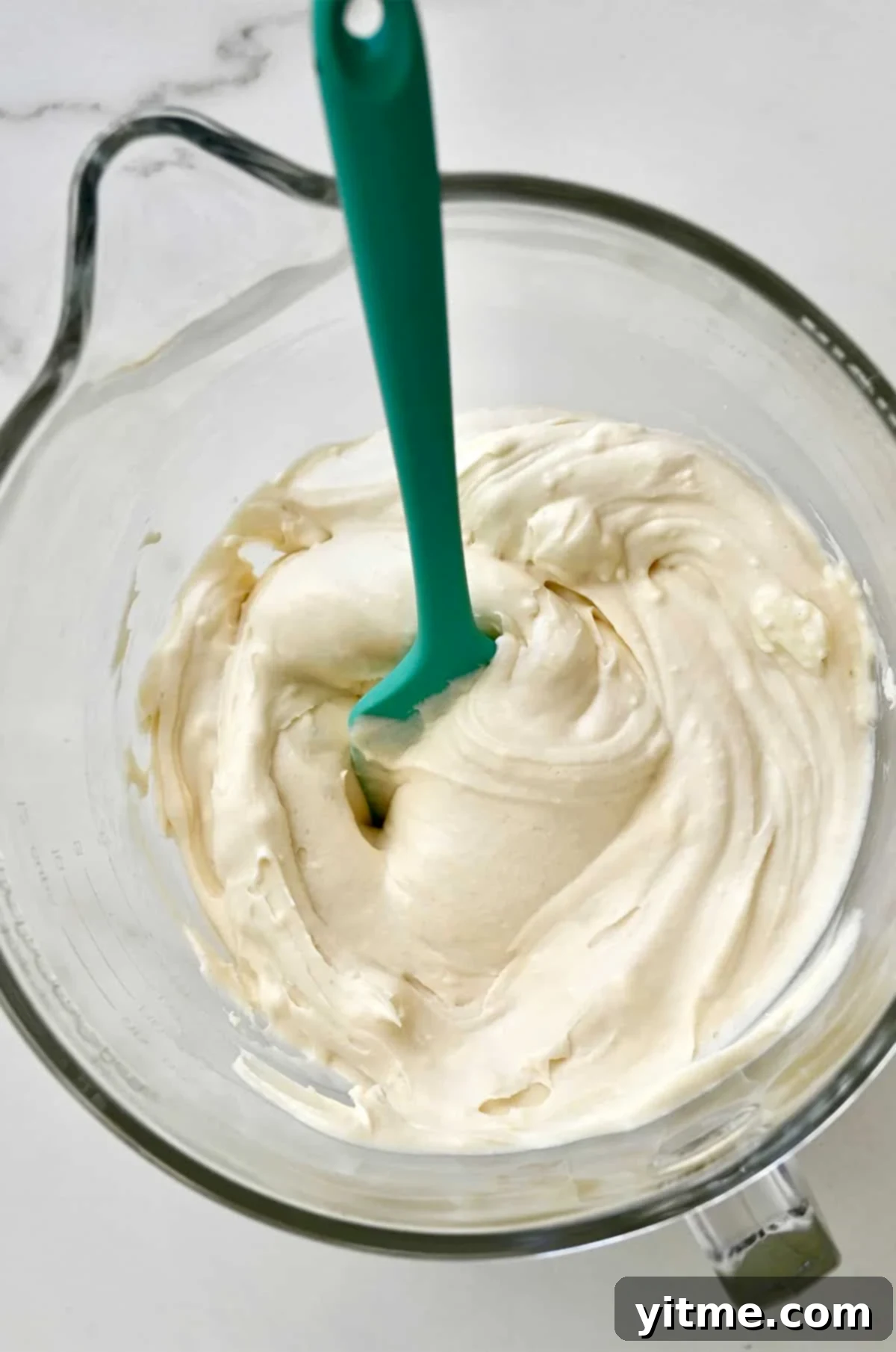 Smooth cream cheese frosting in a bowl with a spatula.