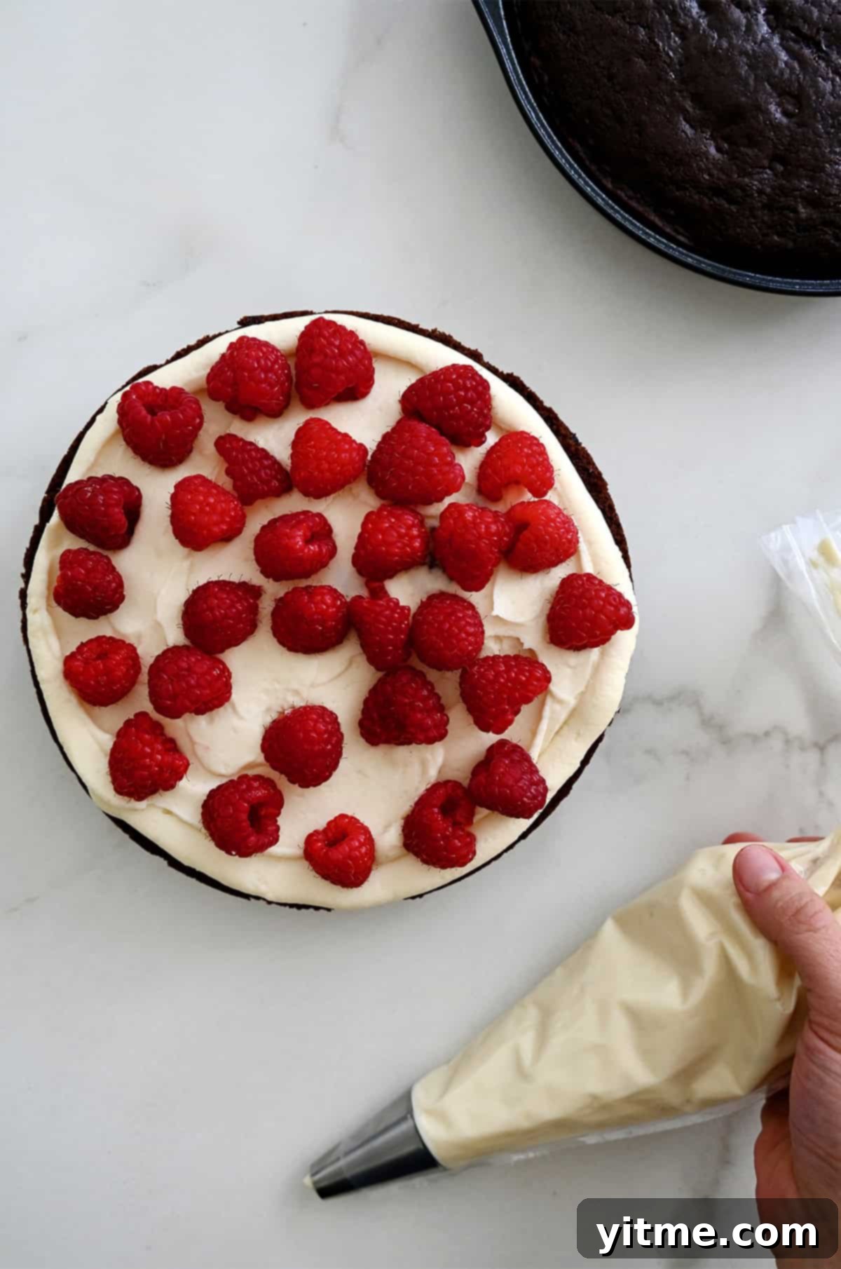 Layering chocolate cake with cream cheese frosting and fresh raspberries.