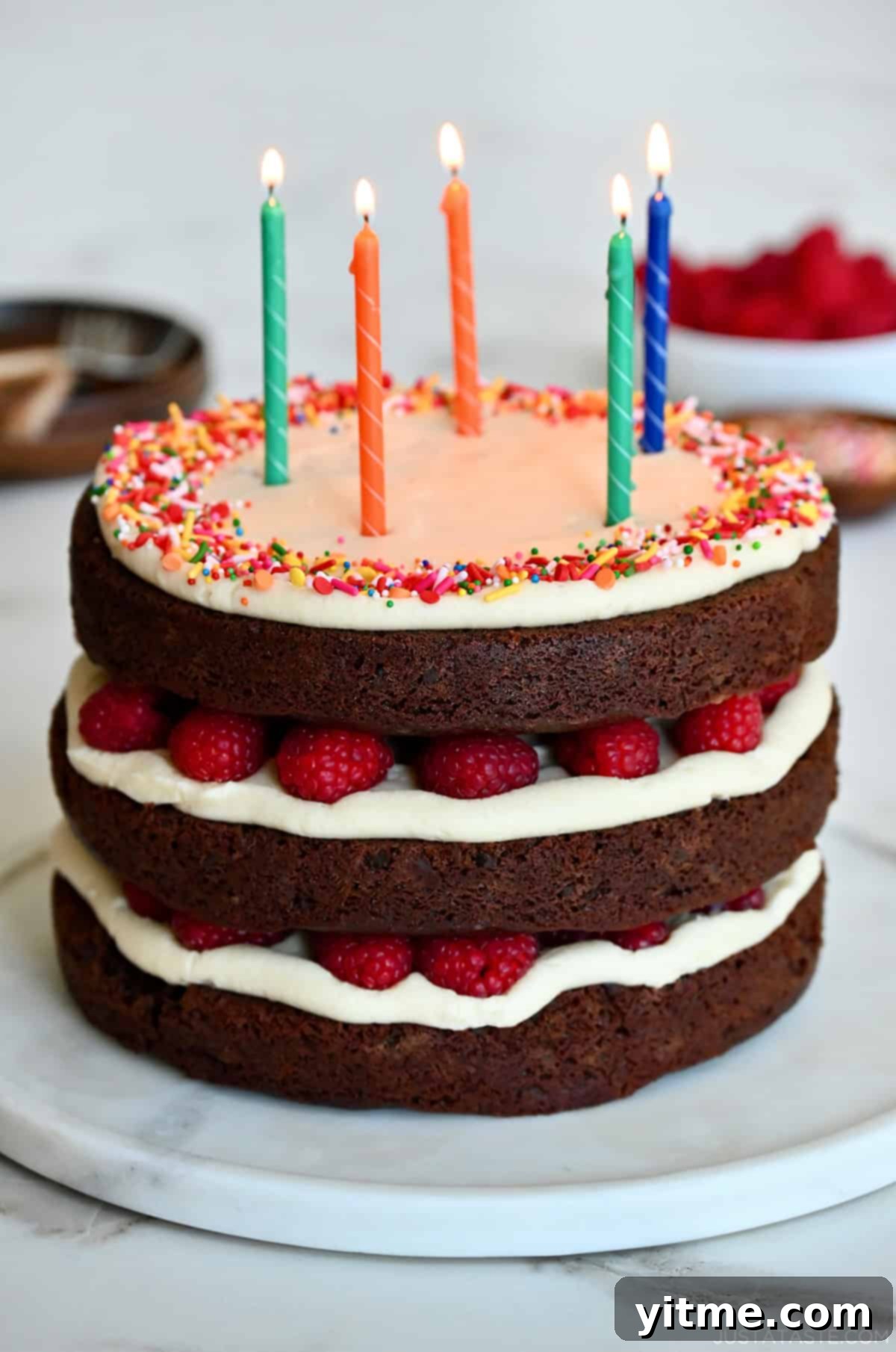A 3-layer chocolate cake with cream cheese frosting and raspberries topped with five candles.