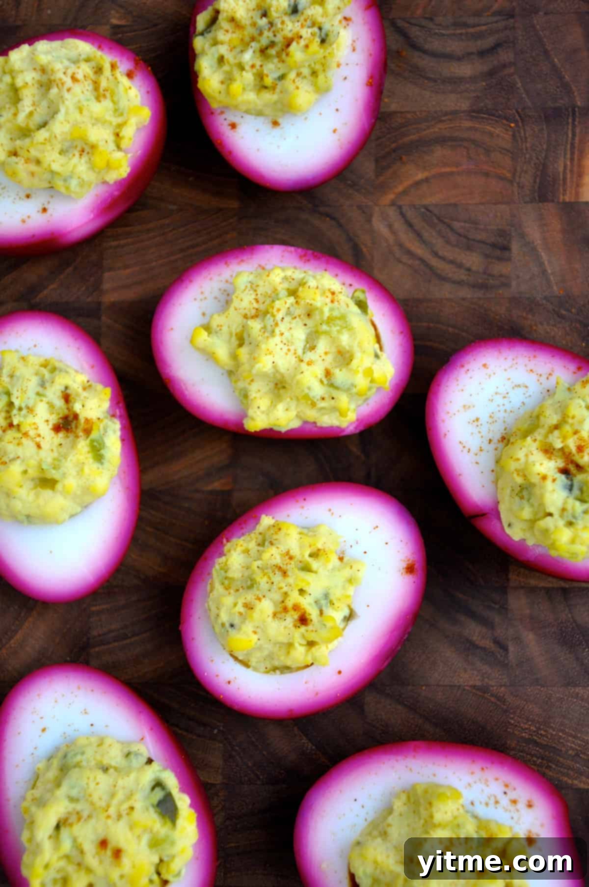 Pickled deviled eggs, naturally dyed with beets, arranged on a wooden surface.