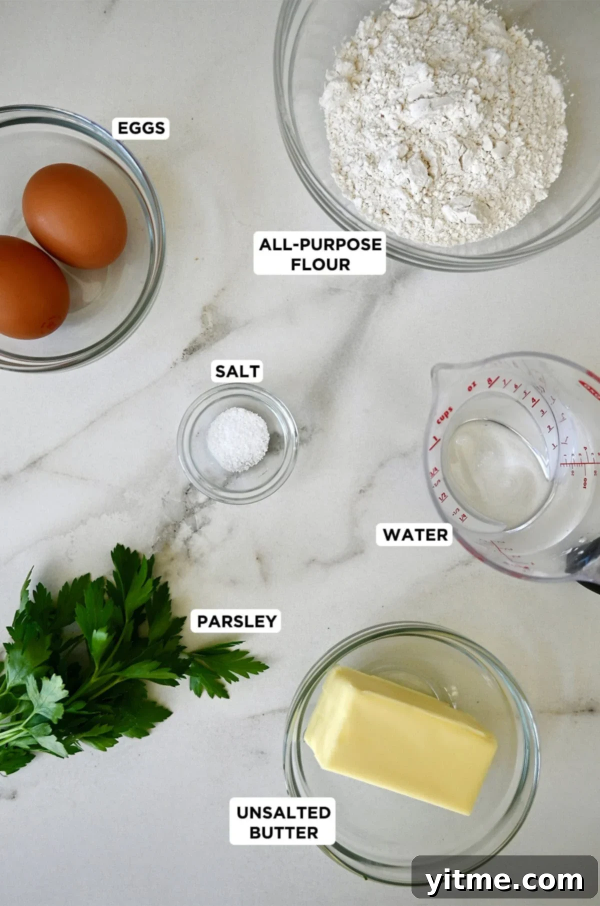 Glass bowls containing eggs, salt, all-purpose flour, water and butter next to a bunch of parsley.