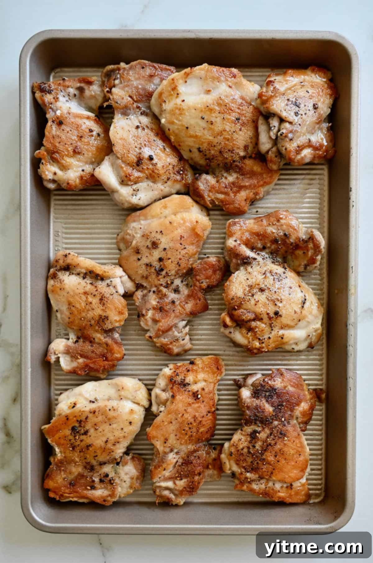 Browned chicken thighs on a baking sheet.