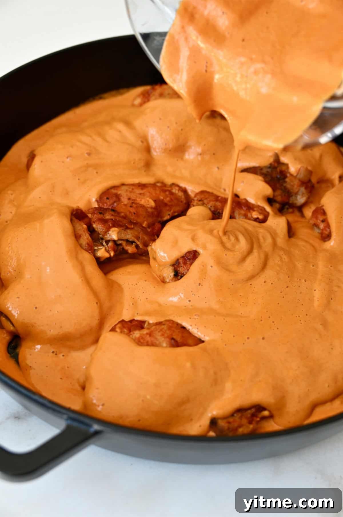 Creamy paprika sauce being poured over braised chicken.