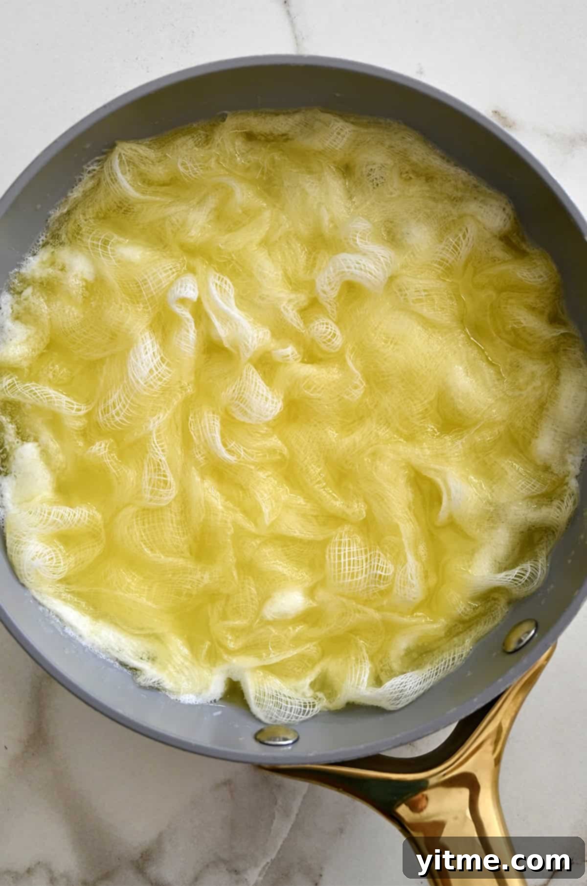 A cheesecloth soaking up melted butter in a large skillet, preparing for a self-basting butter blanket.