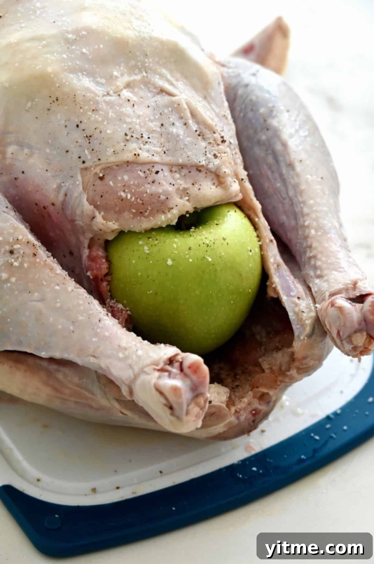 A whole Granny Smith apple propping open the cavity of a turkey, ensuring air circulation during roasting.