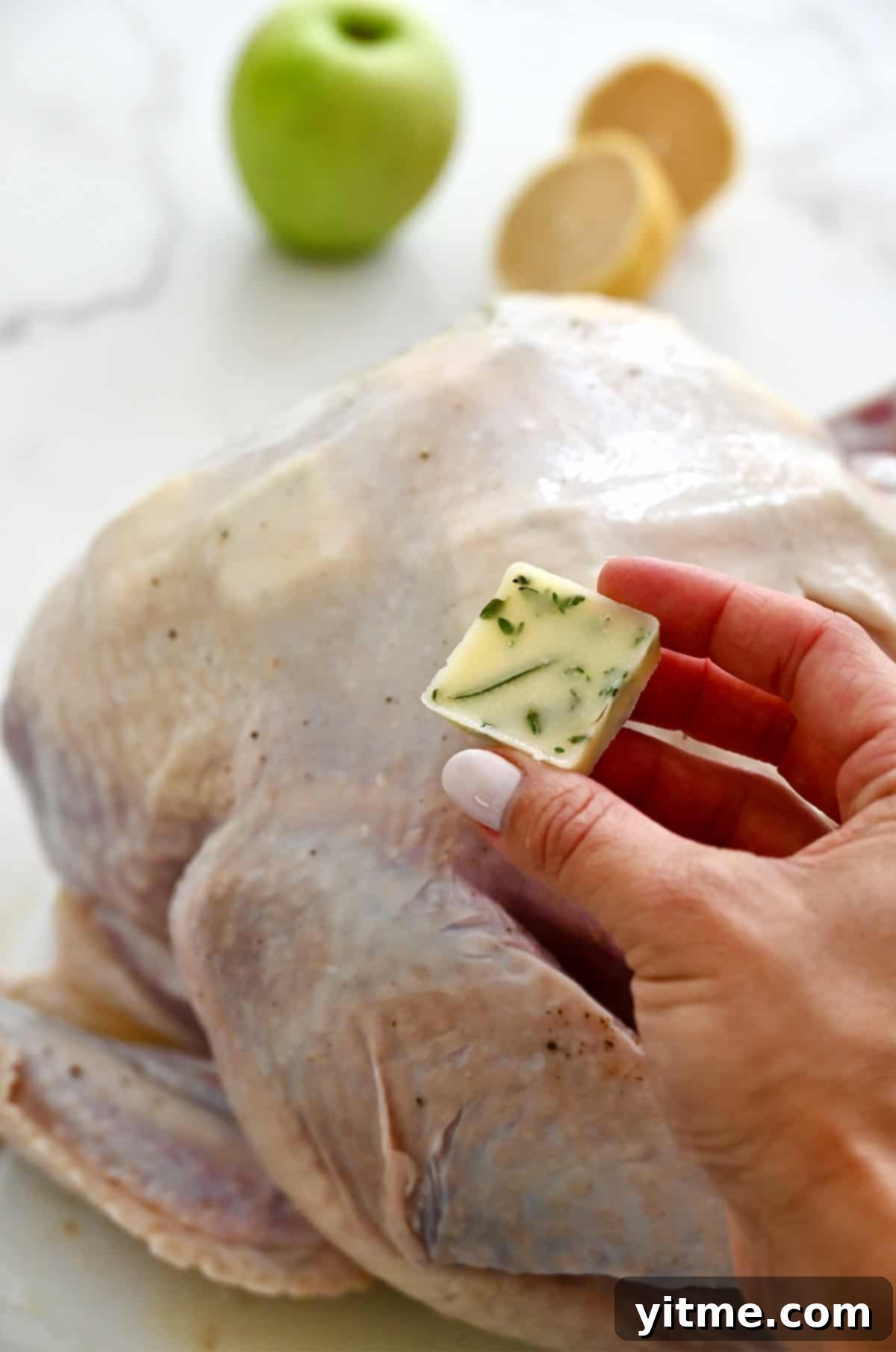 Frozen butter cubes being placed underneath the skin of an uncooked turkey, helping to keep the breast meat moist during roasting.