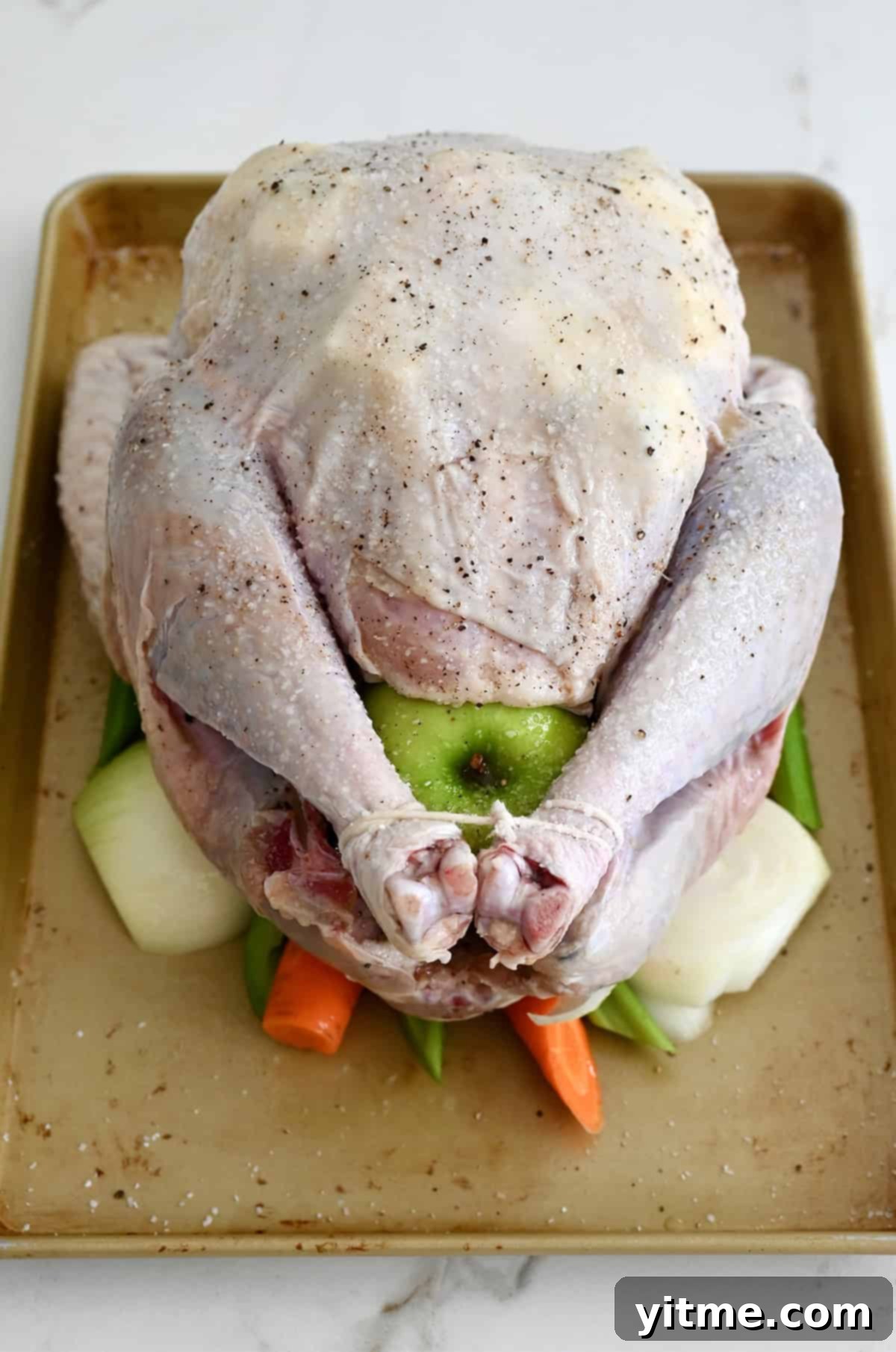 An uncooked turkey atop chopped veggies on a baking tray before roasting, ready to be transformed into a Thanksgiving centerpiece.