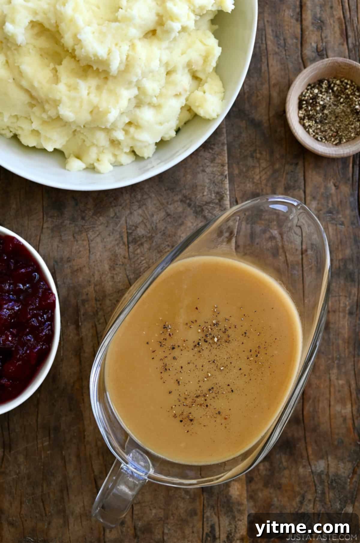 Homemade gravy in a gravy boat next to a bowl with cranberry sauce and a bowl of mashed potatoes.