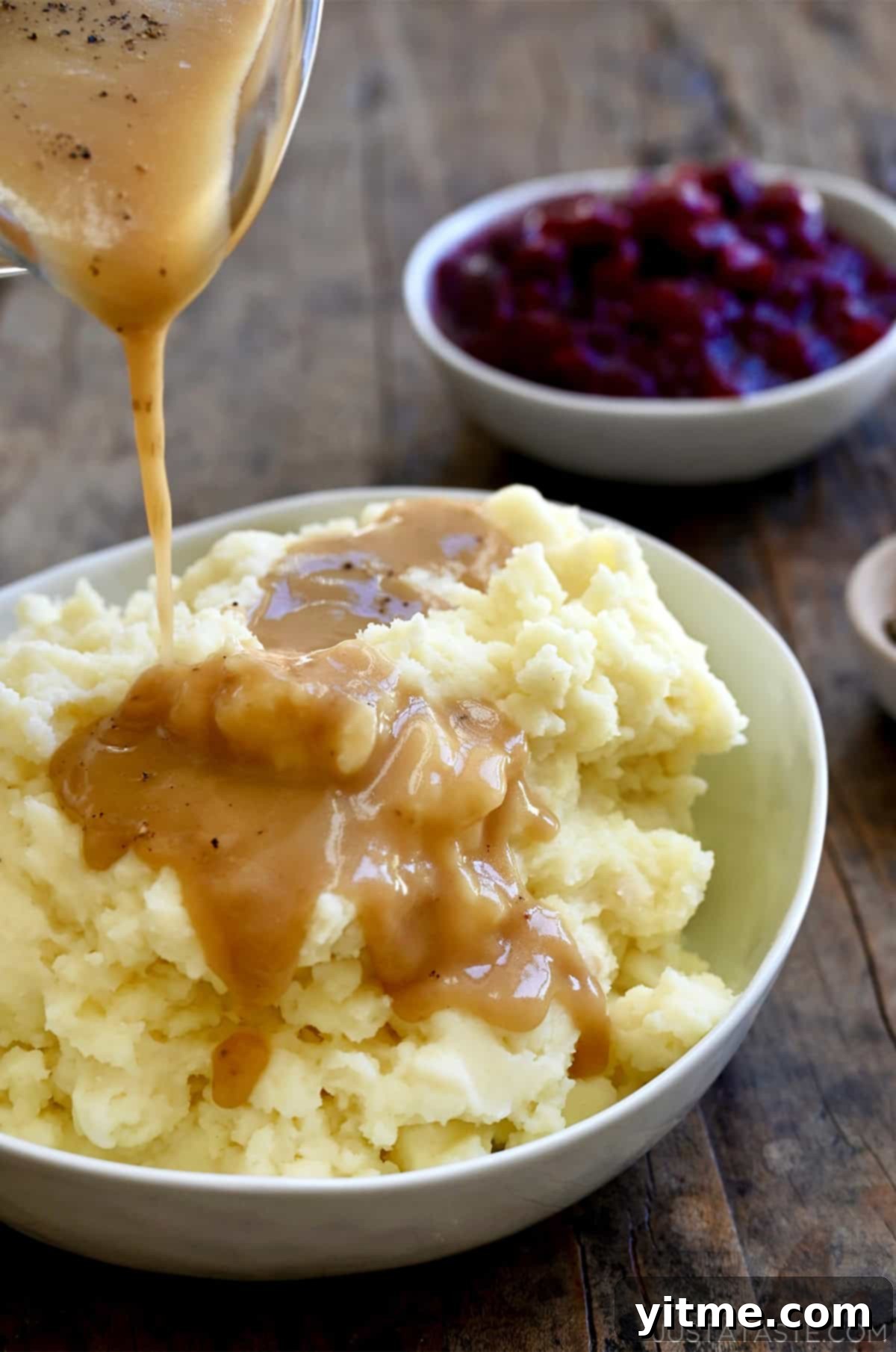 Homemade gravy being poured over mashed potatoes in a large serving bowl.