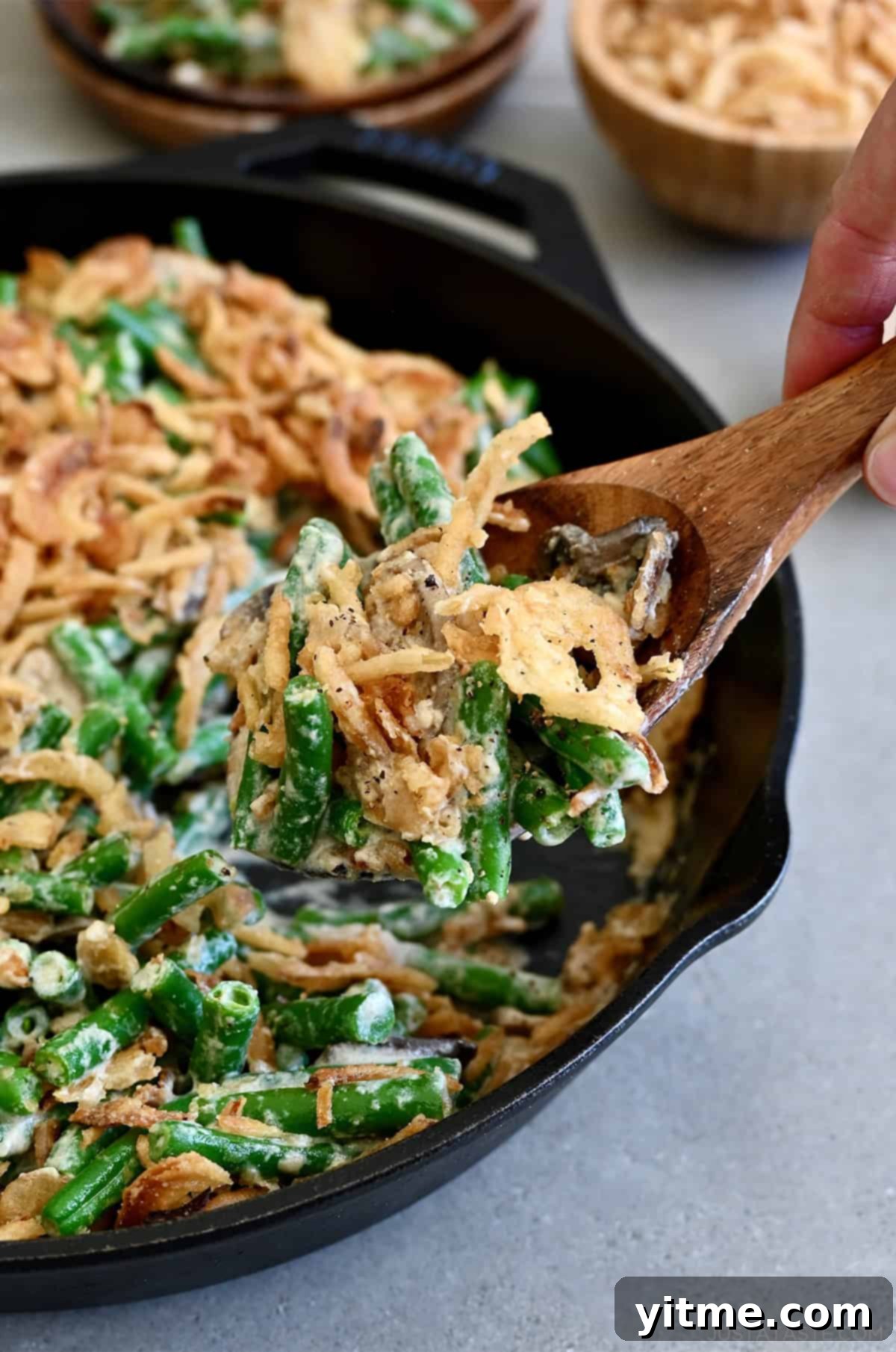 Scooping homemade creamy green bean casserole from a skillet, showcasing its rich texture.