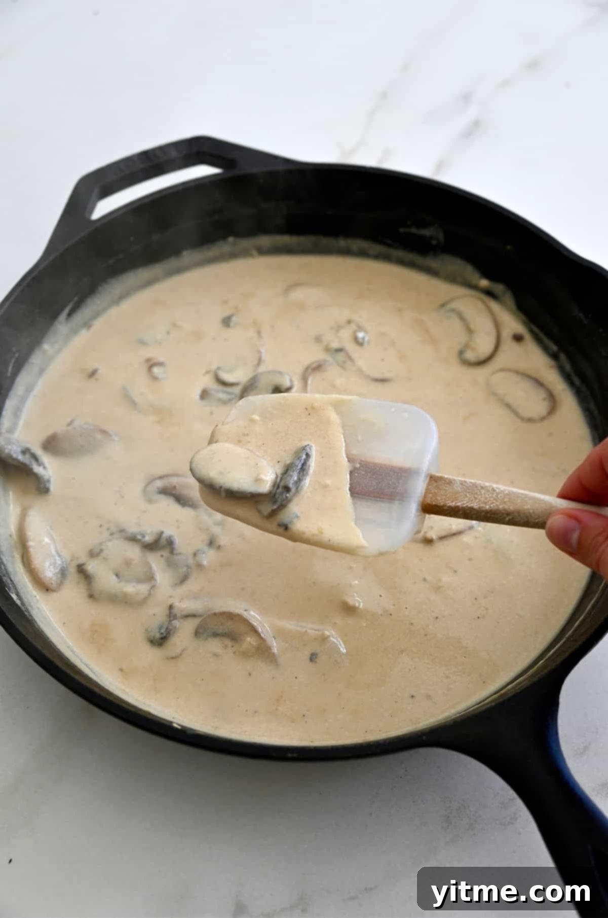 Homemade cream of mushroom soup in a skillet, thick enough to coat a spatula.