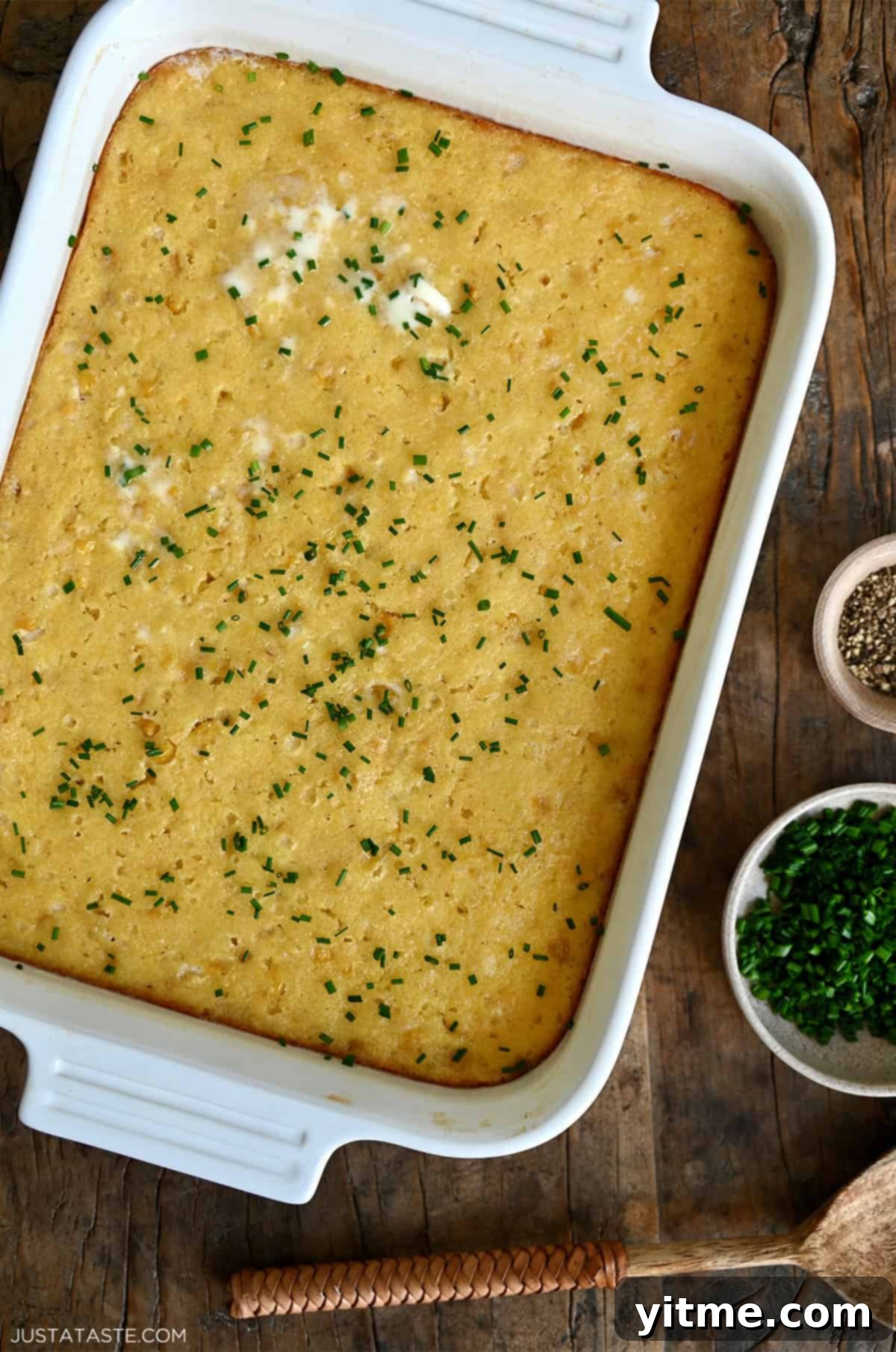 A creamy, golden-brown corn casserole baked in a 9x13 baking dish, ready to be served, with steam subtly rising from its warm surface.
