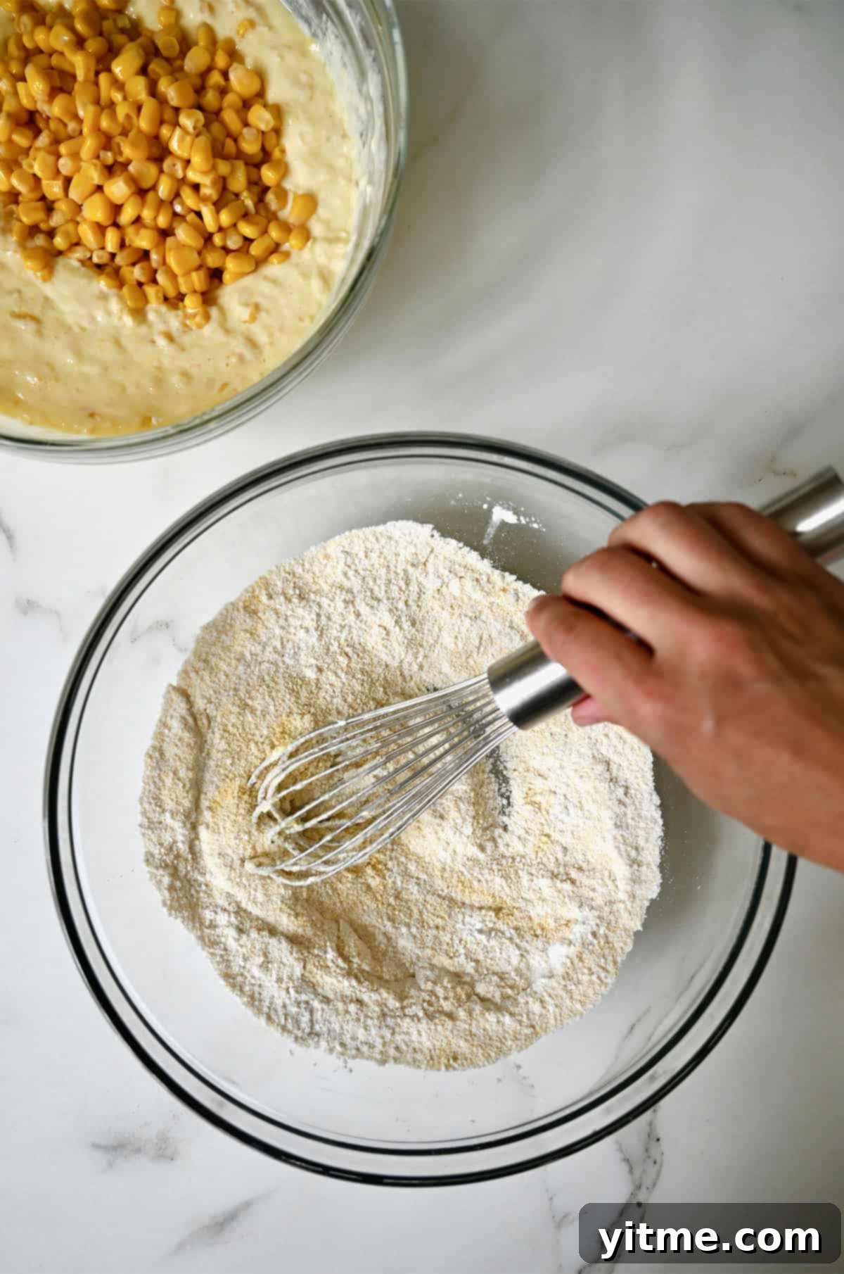 Two separate bowls: one with dry ingredients and another with whisked wet ingredients (melted butter, sour cream, eggs, creamed corn, whole kernel corn) for homemade corn casserole.