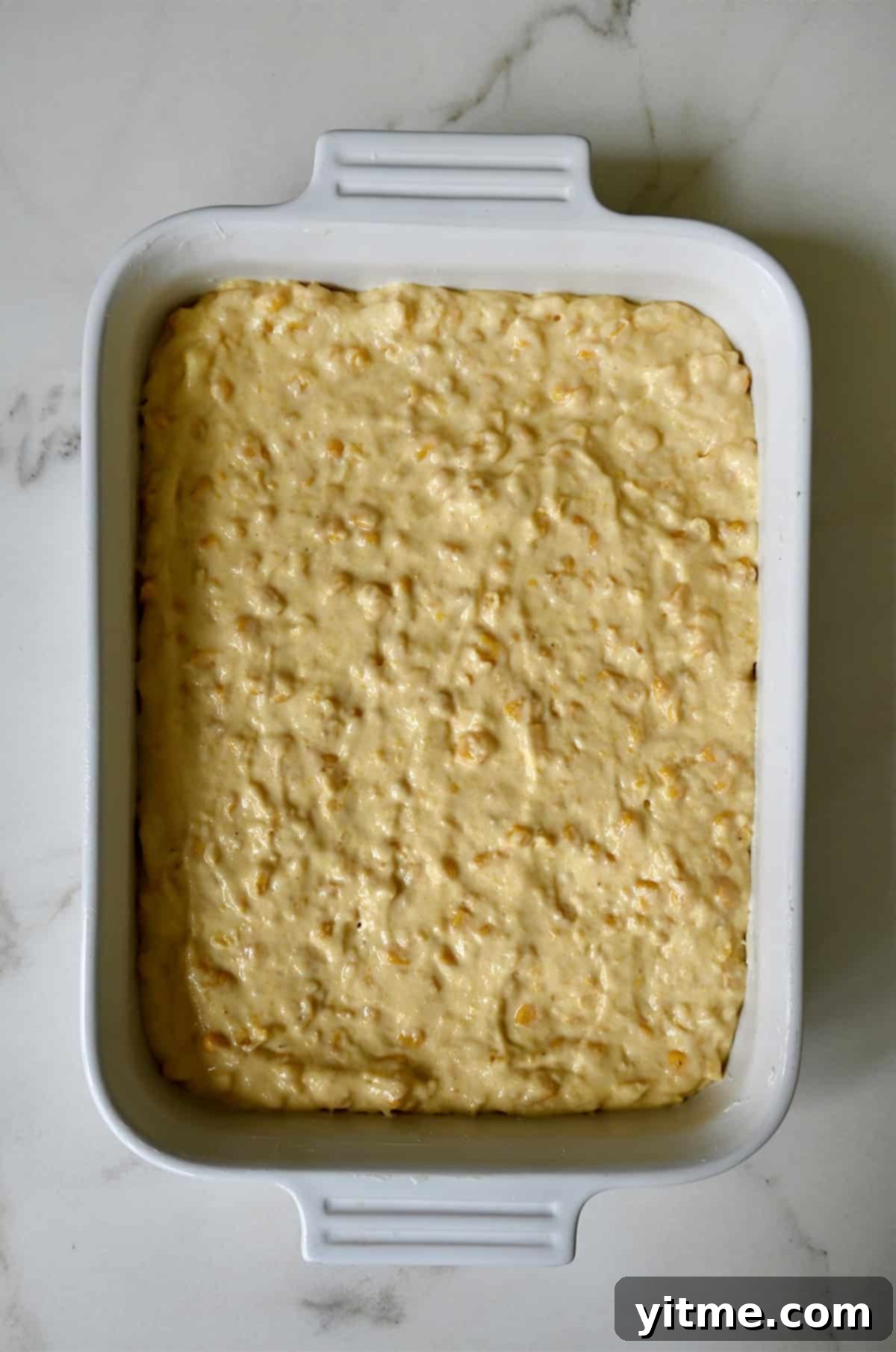 The smooth corn casserole batter carefully scraped into a buttered casserole dish, ready for baking.
