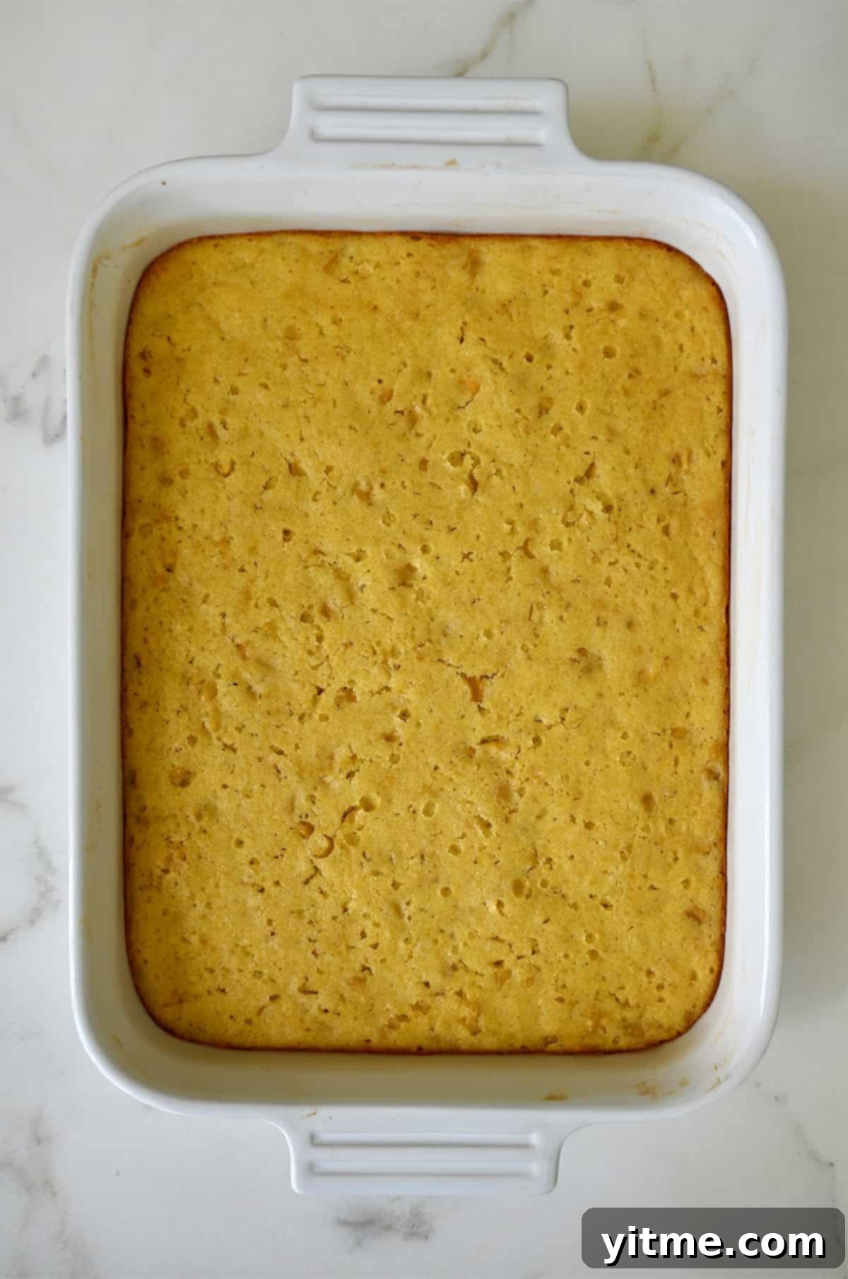 A freshly baked, golden-brown homemade corn casserole in a white baking dish, exhibiting a fluffy texture and slightly crisp edges.