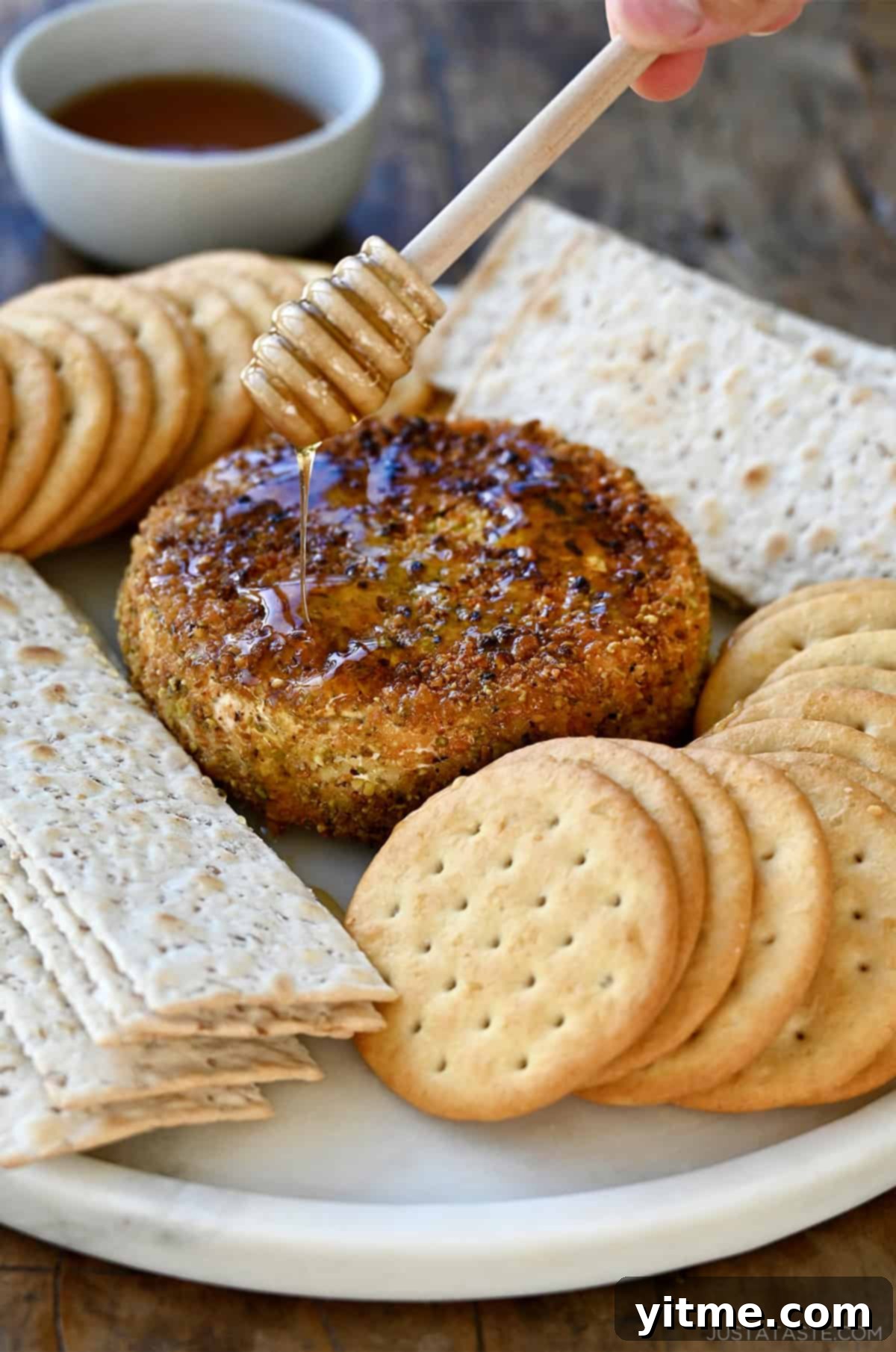 Fried Brie wheel drizzled with honey on a plate surrounded by crackers.
