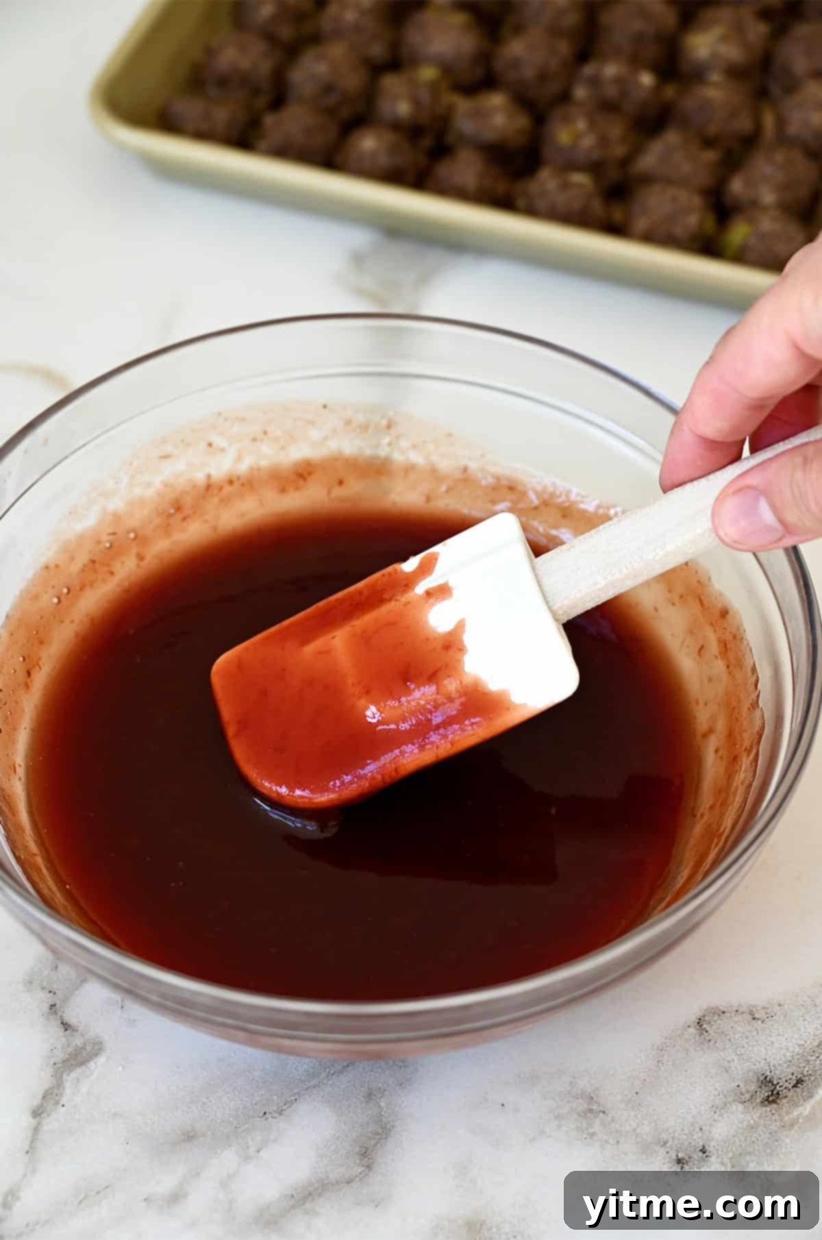 Grape jelly and chili sauce in a  bowl and coating a spatula.