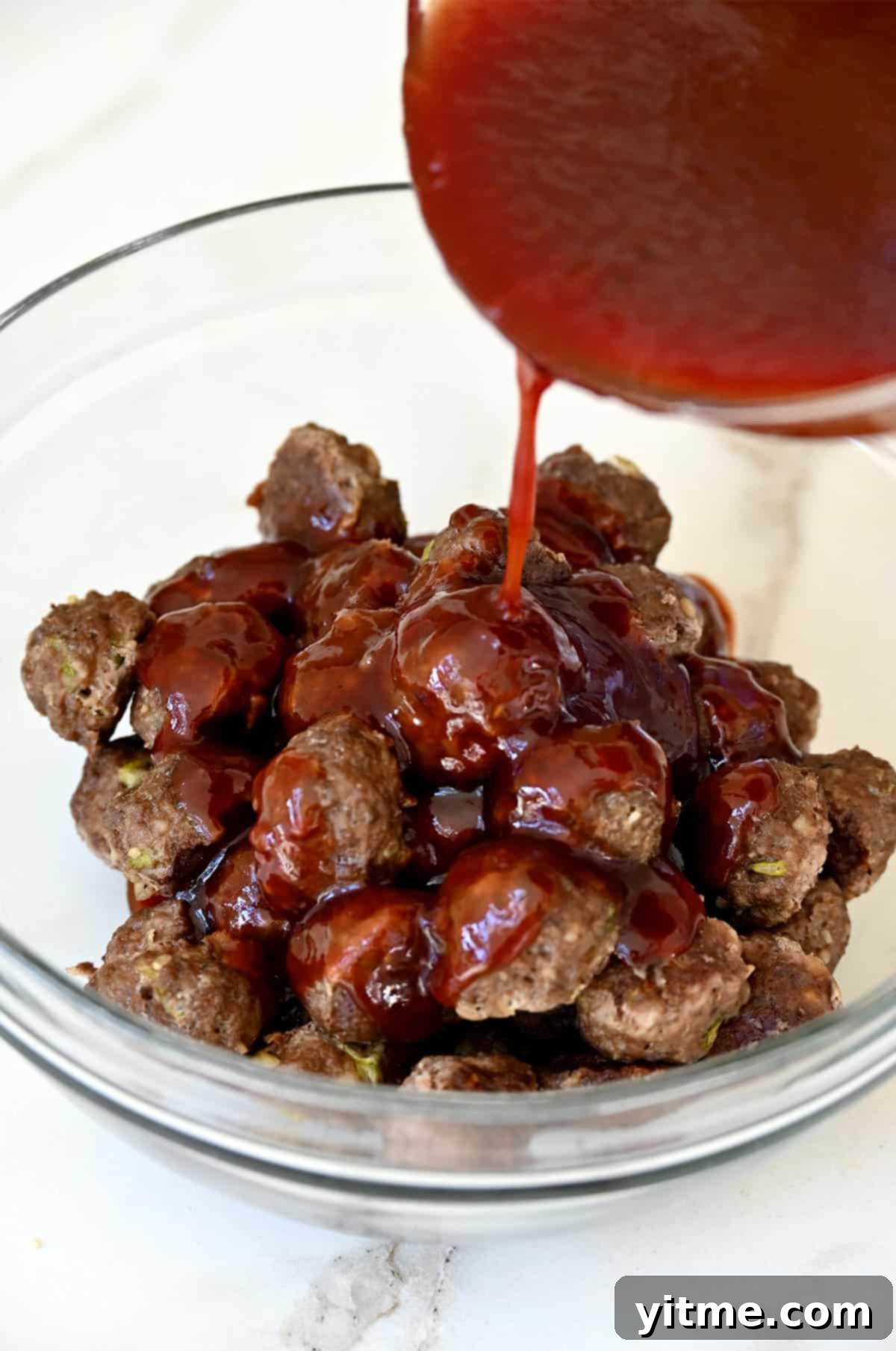 Tossing baked meatballs with grape jelly sauce in a bowl.