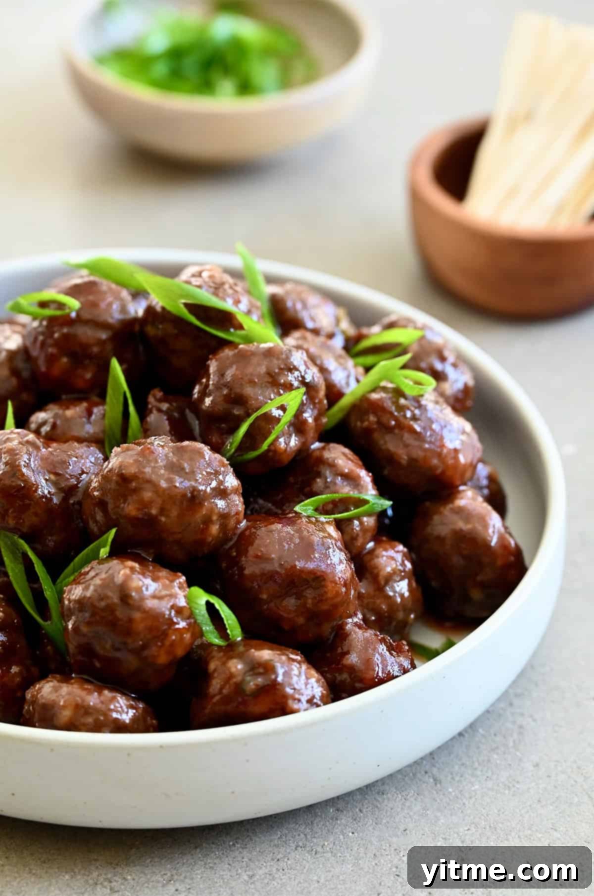 Grape jelly meatballs made from scratch in a bowl garnished with sliced scallions.