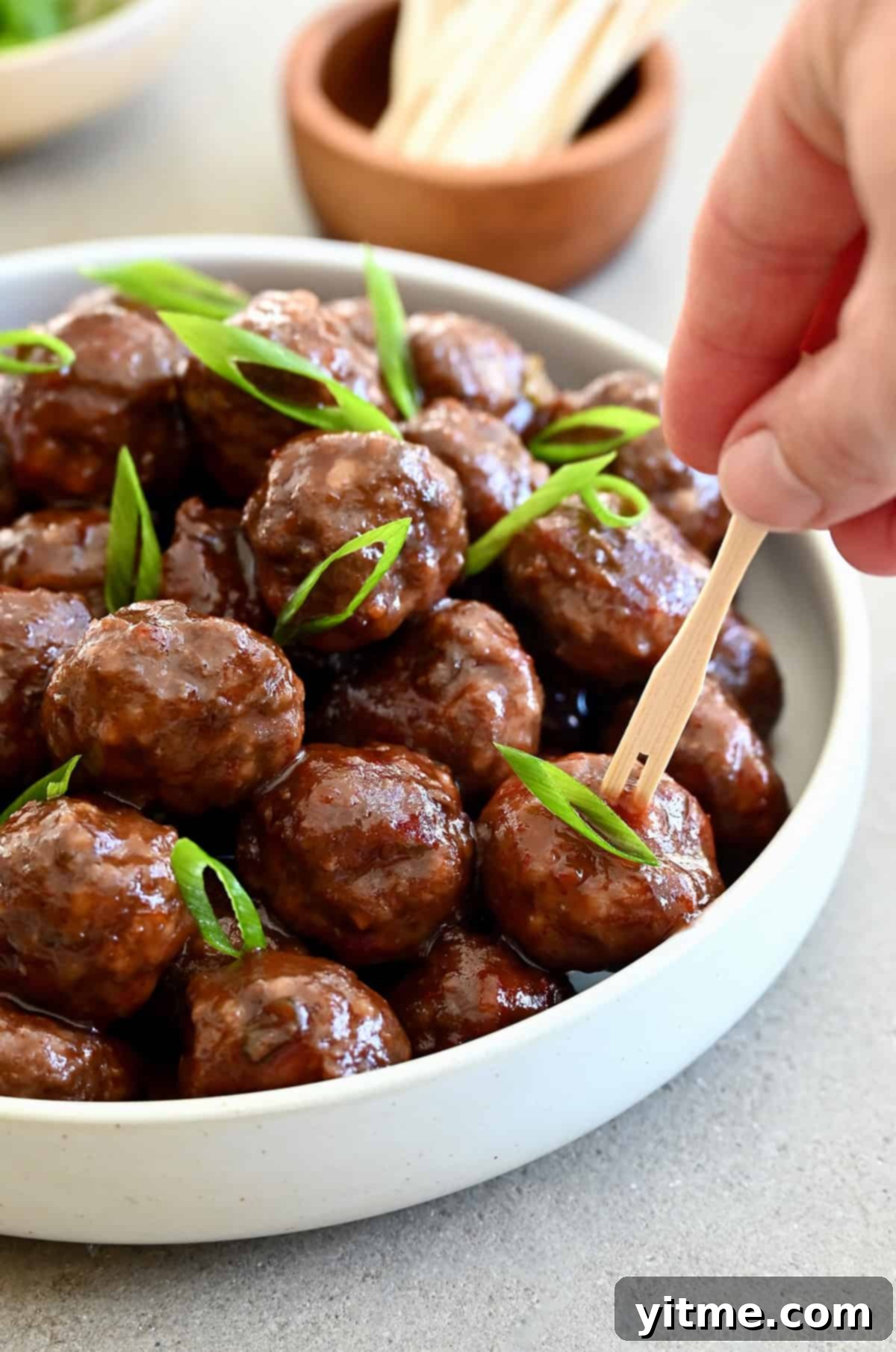 Grape jelly cocktail meatballs in a bowl with toothpicks nearby for serving.