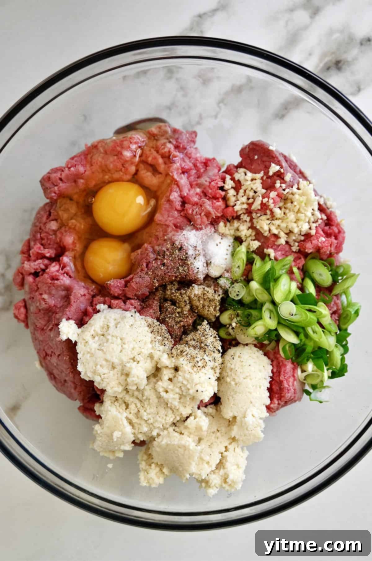 Panade, ground beef, eggs, minced garlic, sliced scallions, salt and pepper in a glass bowl.