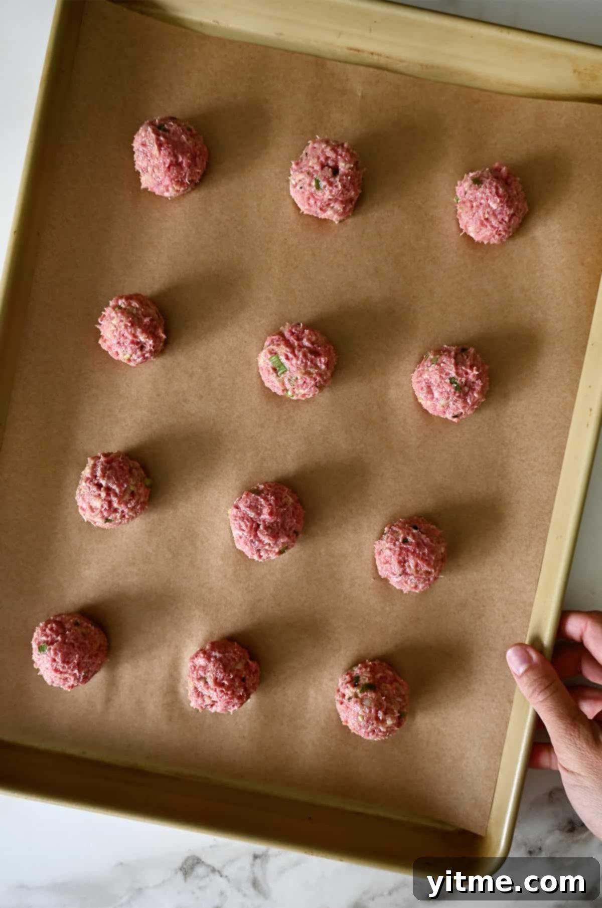 Ground beef cocktail meatballs on a parchment paper-lined baking sheet.