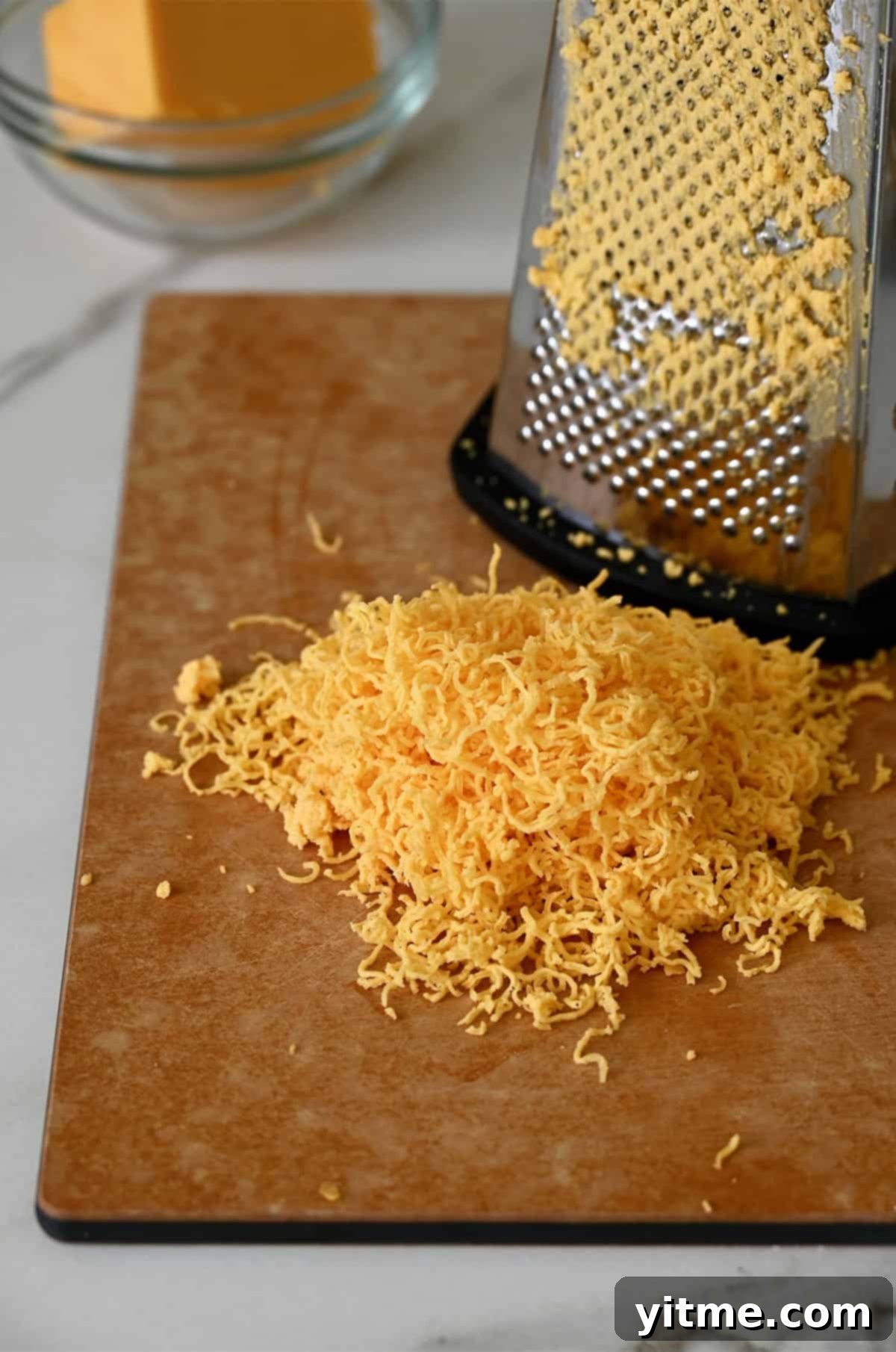 Shredded cheddar cheese on a cutting board.