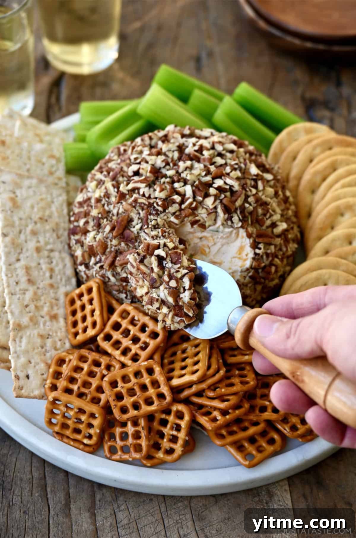 Timeless Cheese Ball 2 A classic cheese ball coated in chopped pecans on a plate surrounded by pretzels and crackers.