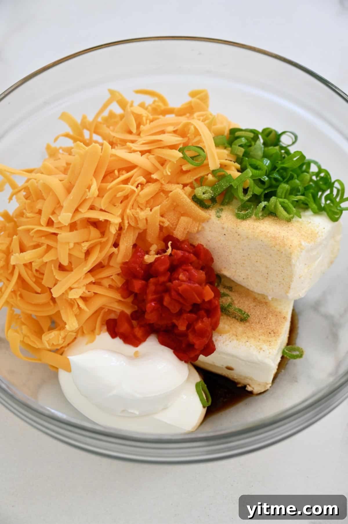 Timeless Cheese Ball 4 Cream cheese, sour cream, shredded cheddar, chopped scallions, pimiento peppers, garlic powder and Worcestershire sauce in a glass bowl.