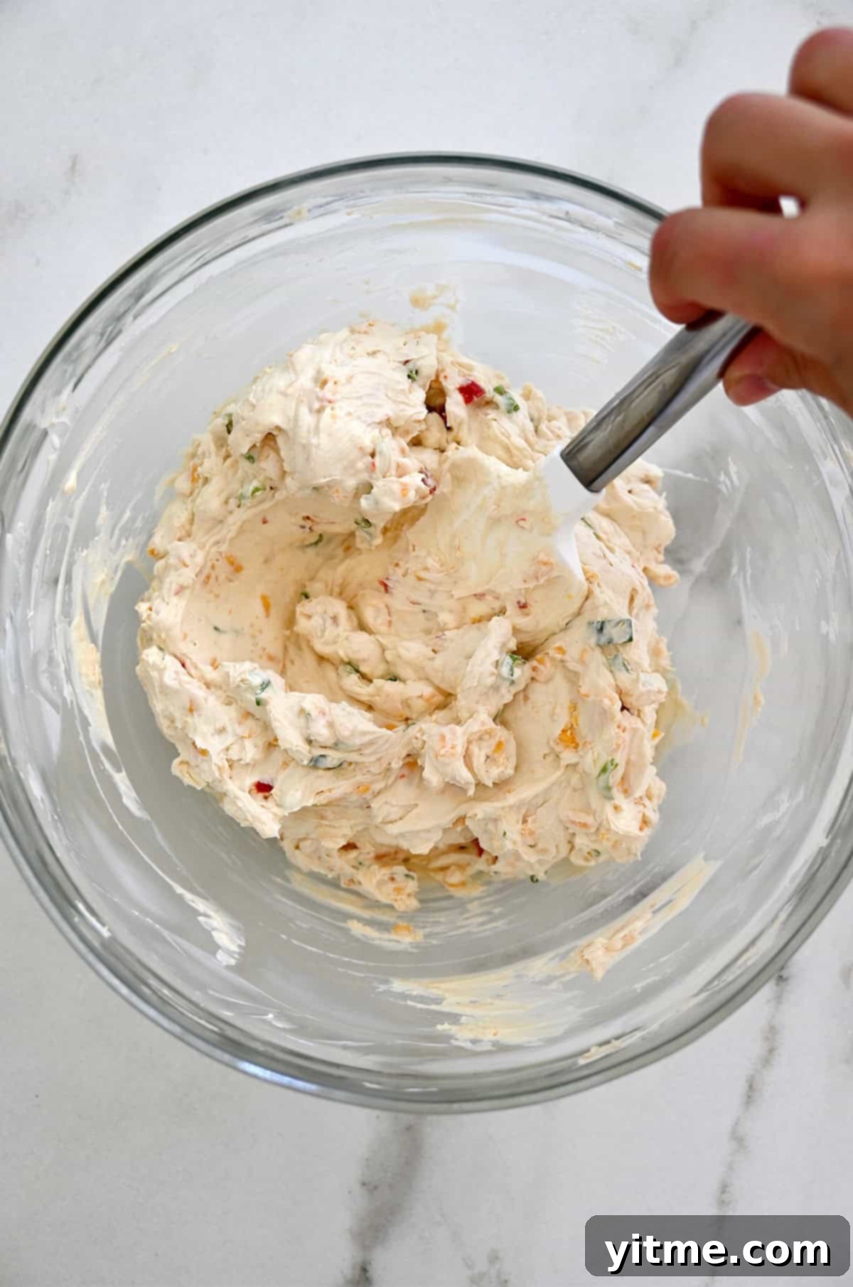 Timeless Cheese Ball 5 Cheese mixture in a glass bowl with a spatula.