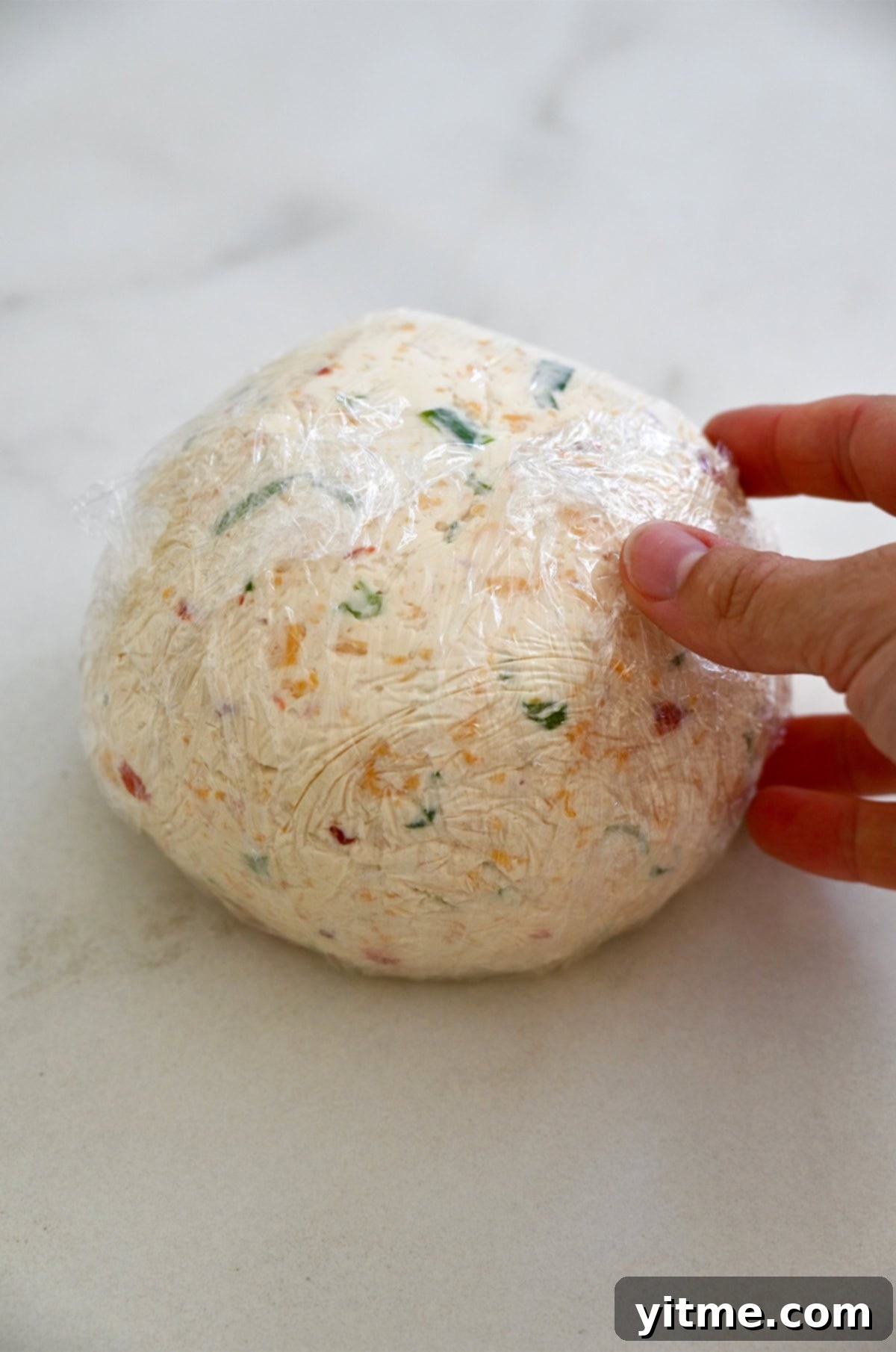 Timeless Cheese Ball 7 Round ball of cheese covered in plastic wrap.