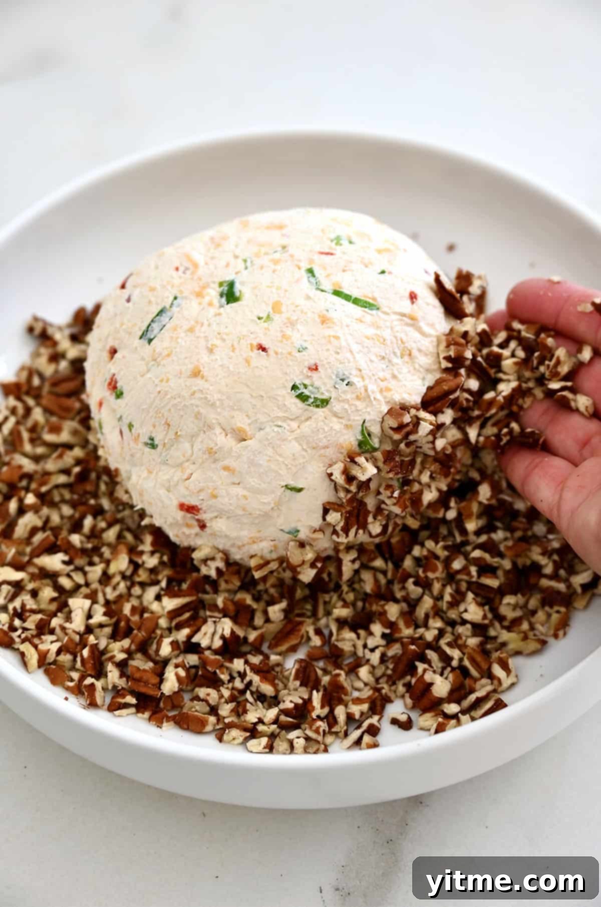 Timeless Cheese Ball 8 A cheeseball sits atop crushed pecans on a plate.