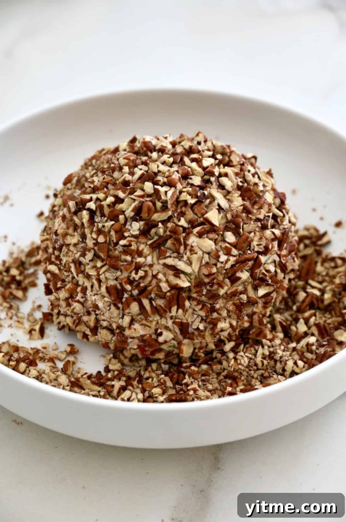 Timeless Cheese Ball 9 A cheese ball coated in chopped pecans on a shallow plate.