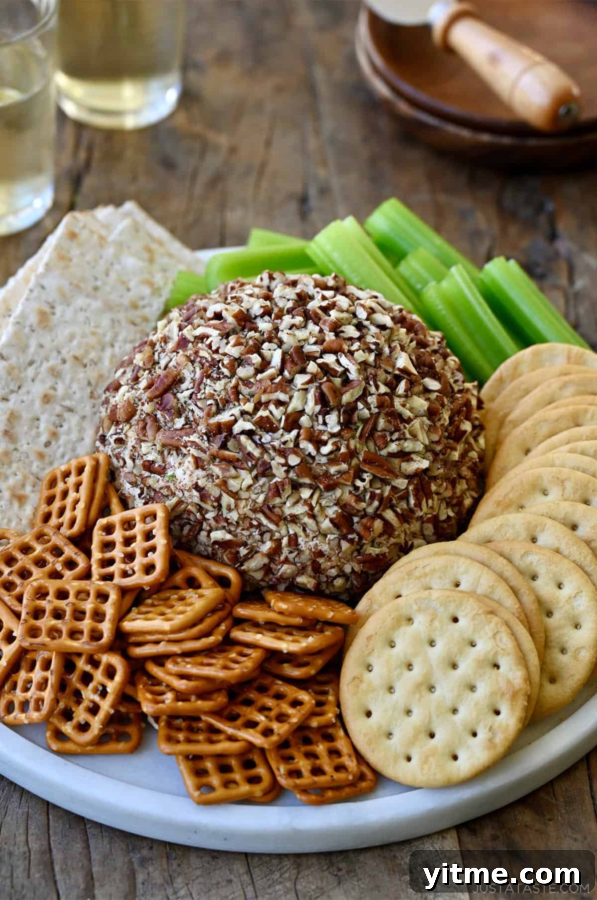 Timeless Cheese Ball 10 Cheese ball coated in crushed pecans on a serving plate with mini pretzels, crackers and celery sticks.