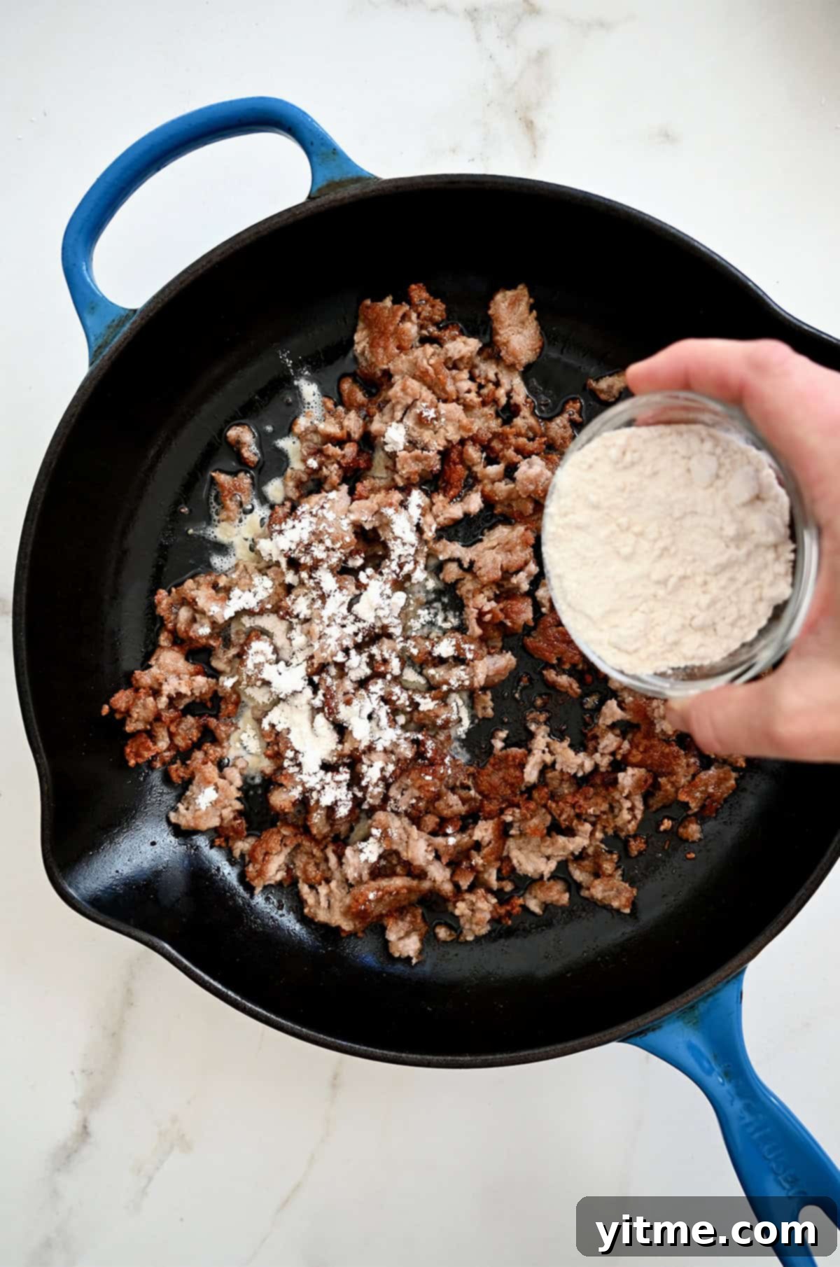 Adding flour to browned sausage in a skillet
