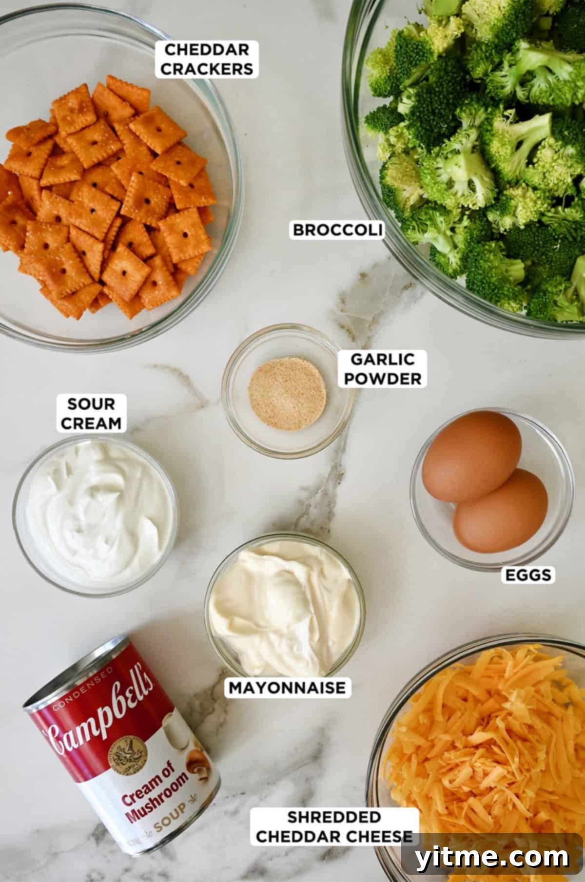 Ingredients to make broccoli casserole, including fresh broccoli florets, shredded cheddar cheese, cream of mushroom soup, eggs, sour cream, mayonnaise, garlic powder, and cheese crackers. Essential for the perfect broccoli cheese casserole.